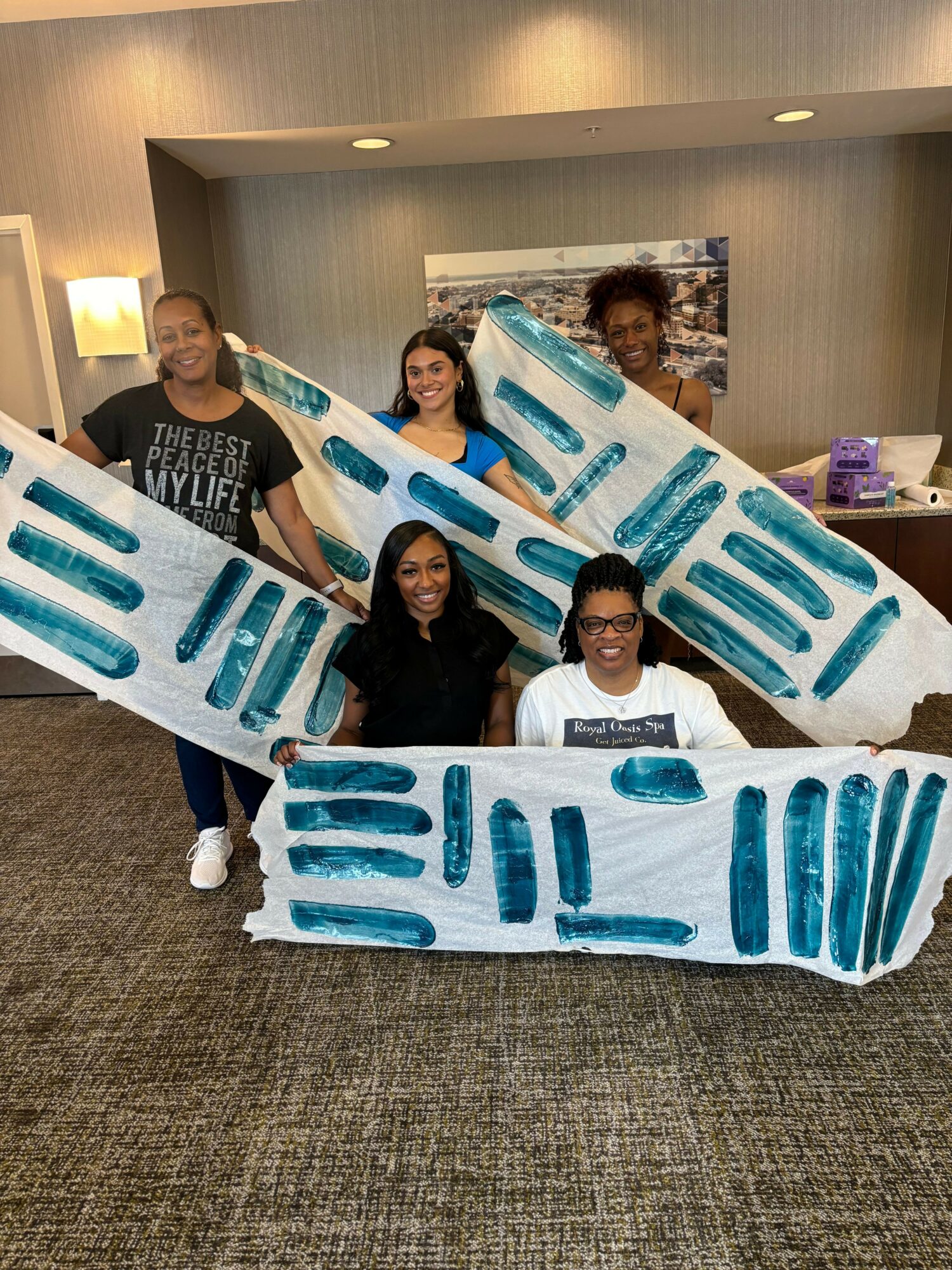 Five women holding large ice-themed banners in an indoor setting with gray walls and carpeted floor.