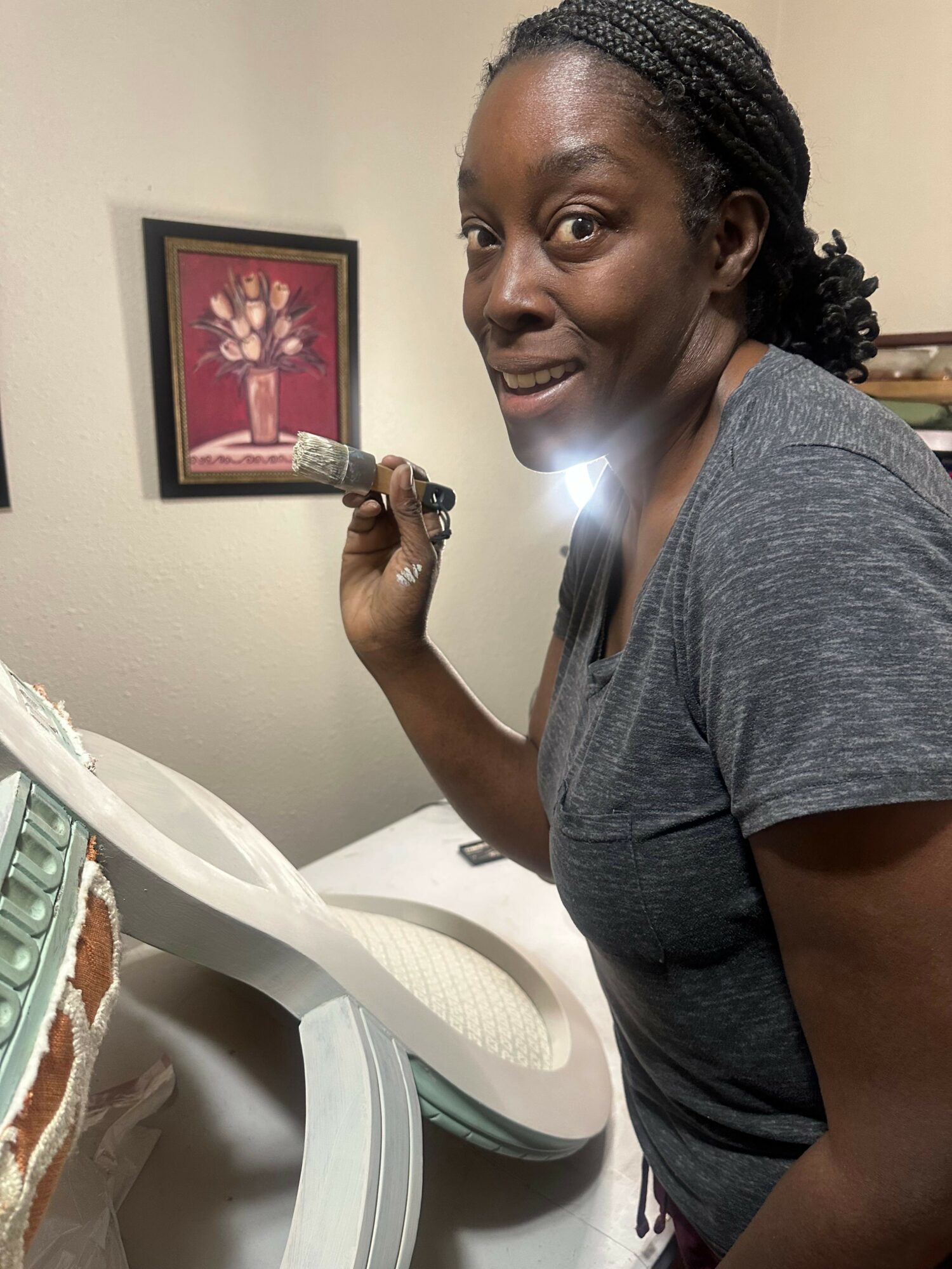 Woman with braided hair smiling, holding a cake knife, in a room with a framed flower picture on the wall.