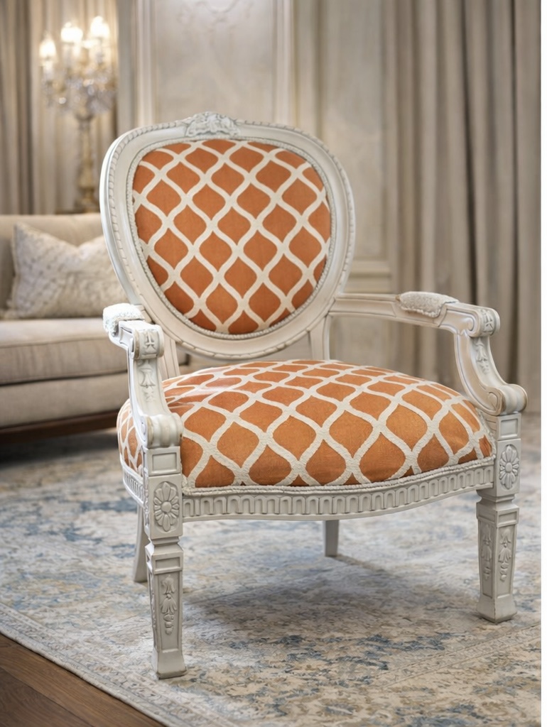 Elegant armchair with orange and white patterned upholstery, carved white wooden frame, in a room with curtains and sofa.