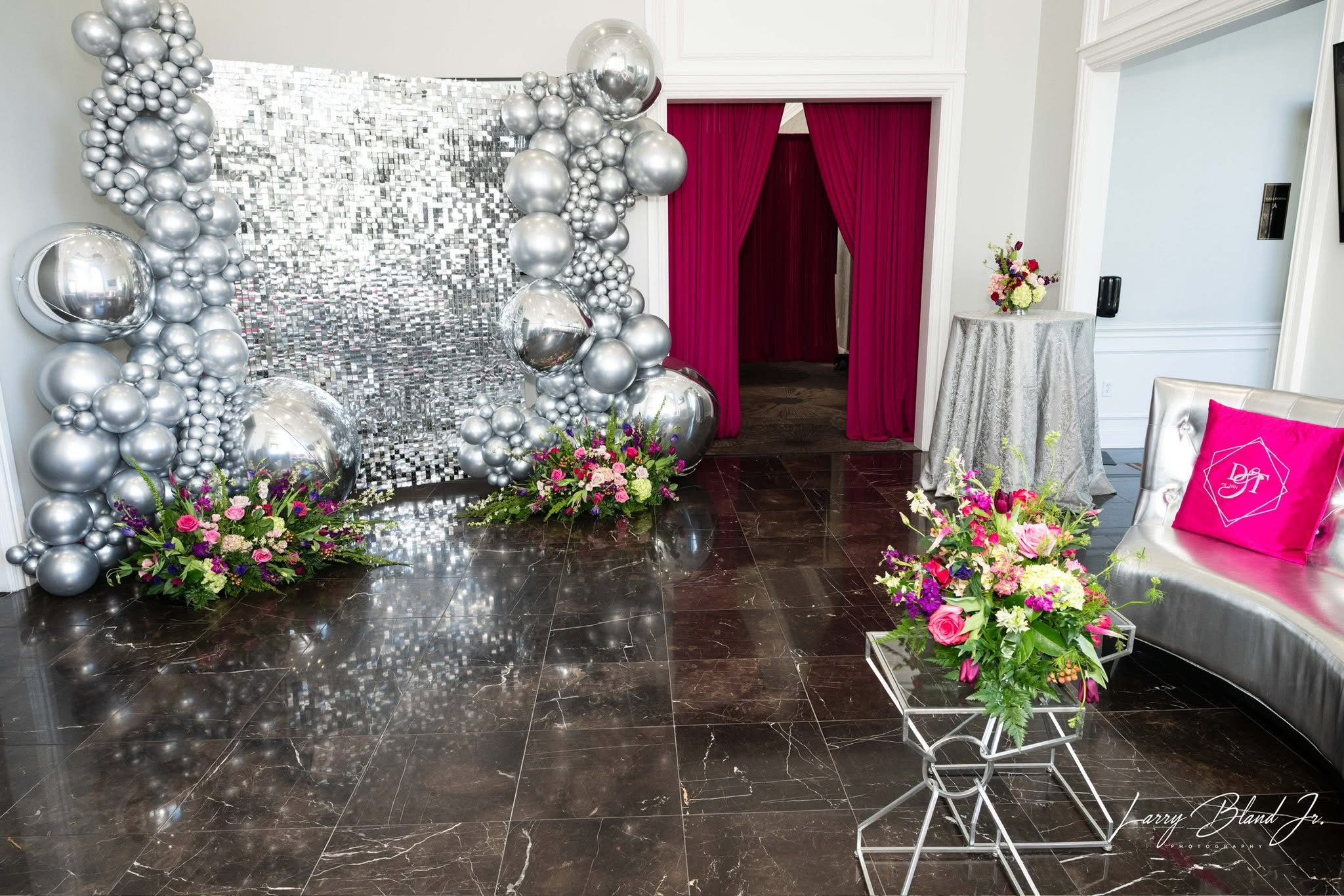 Decorative silver and pink floral arrangements with a silver backdrop and a pink cushion on a bench.
