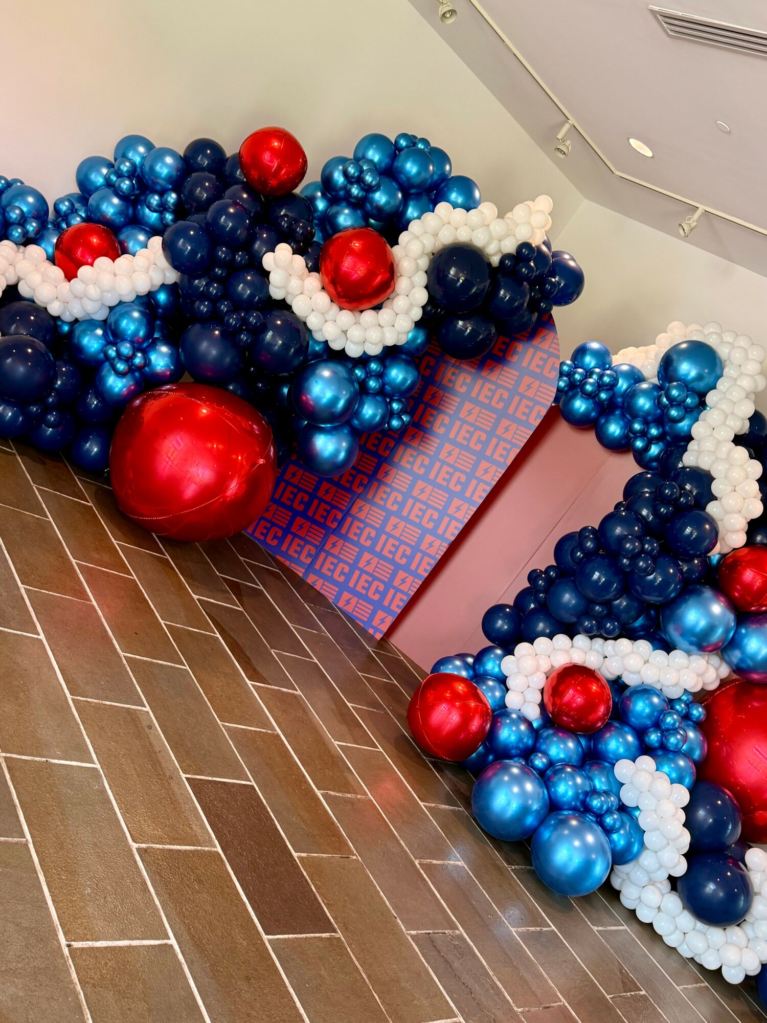 Decorative balloon arrangement with red, blue, and white balloons on a patterned box and wooden floor.