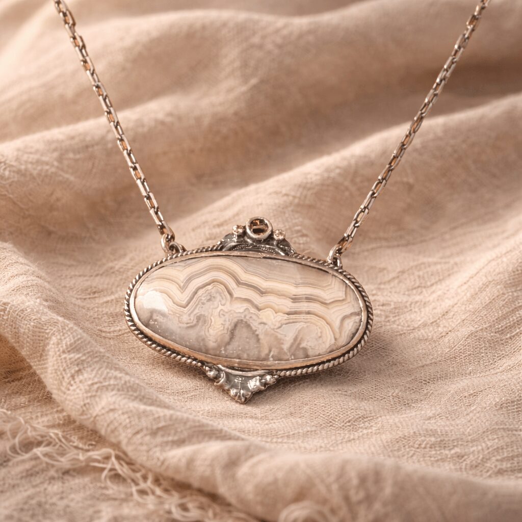 Pendant necklace with an oval stone on a beige fabric background.