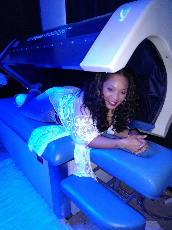 Woman lying on a medical imaging machine bed, smiling, with a large scanner above her head, illuminated by blue light.