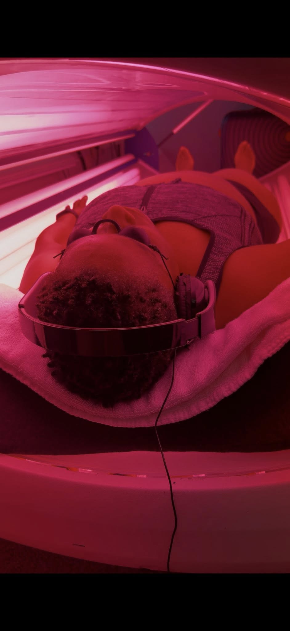 Person lying inside a medical or scientific machine with pink lighting, wearing protective glasses and headphones.