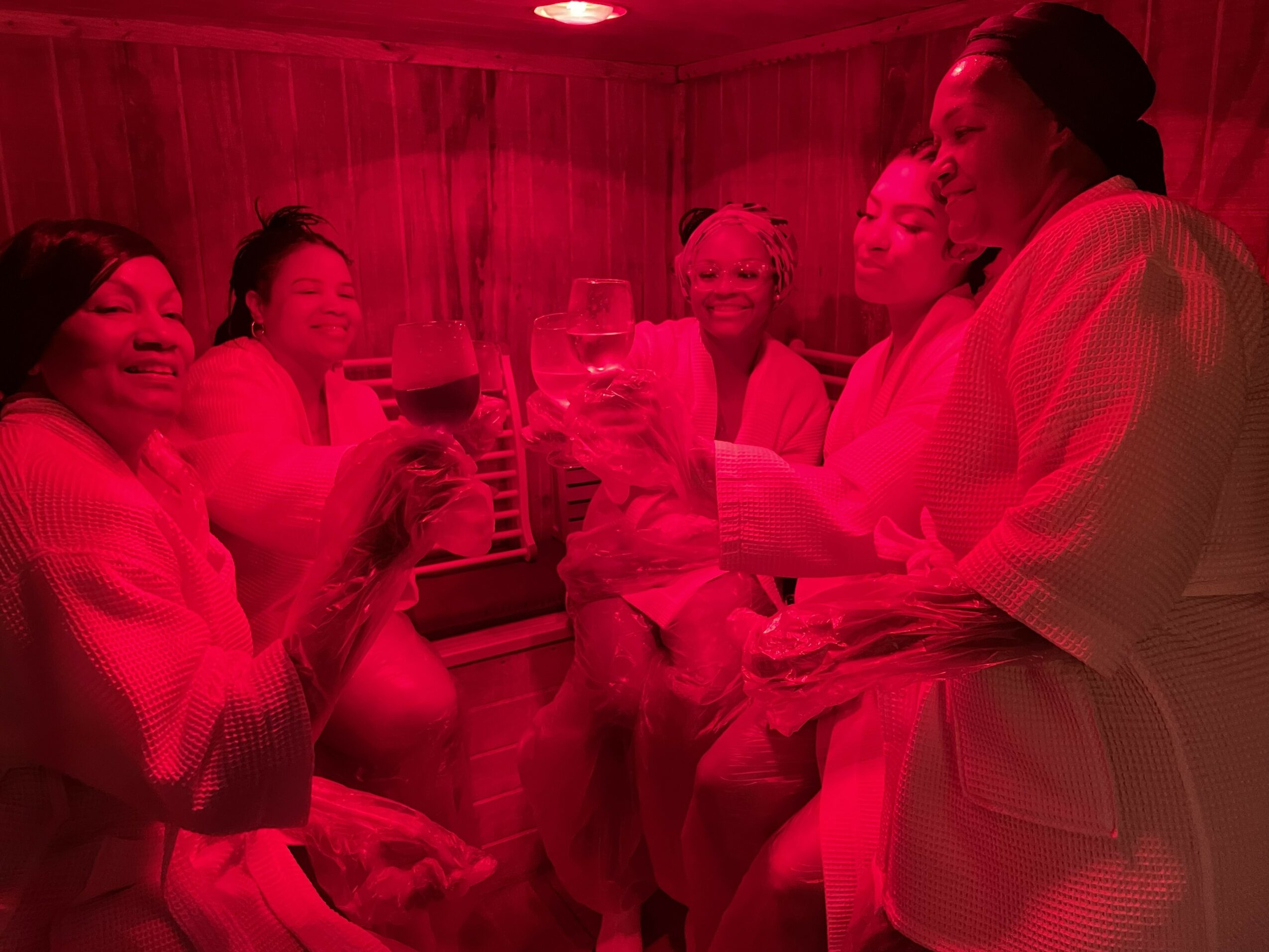 Group of women in robes enjoying drinks in a warmly lit room.
