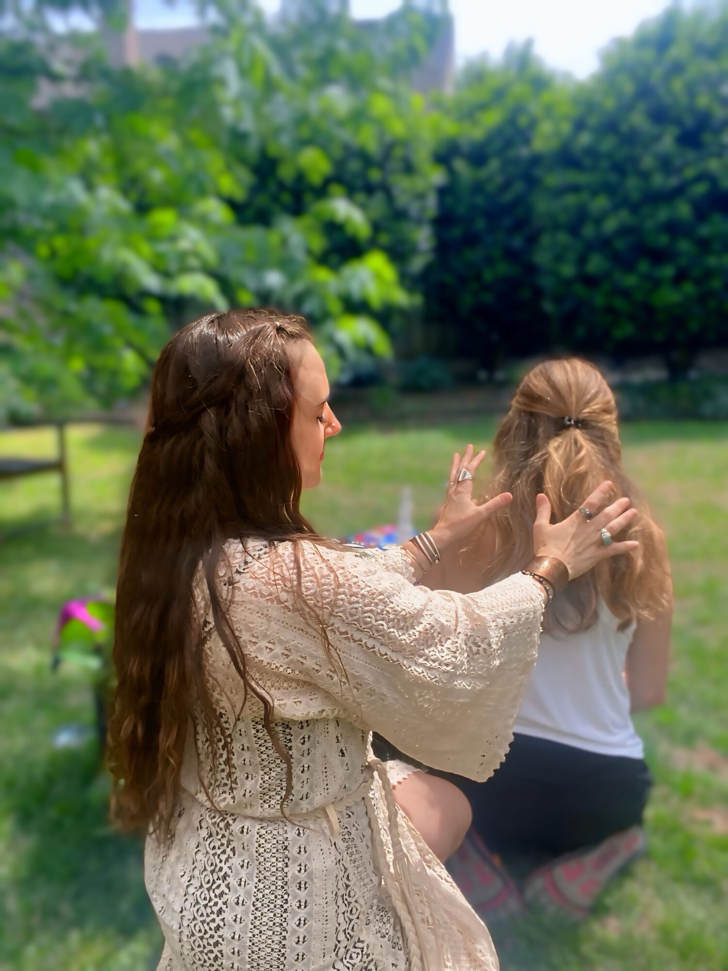 Two women sitting outdoors on grass, one with long brown hair and the other with blonde hair, engaging in conversation.