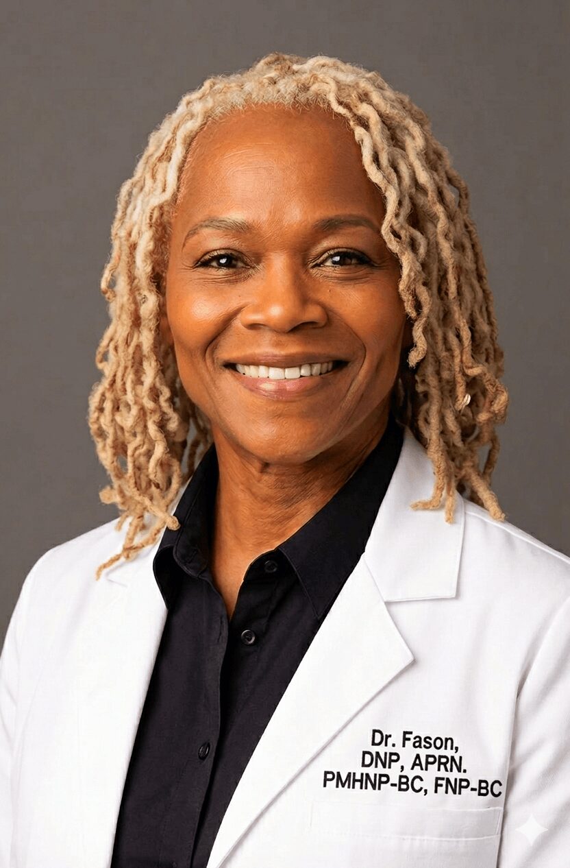 Smiling woman with blonde dreadlocks wearing a white coat and black shirt against a gray background.
