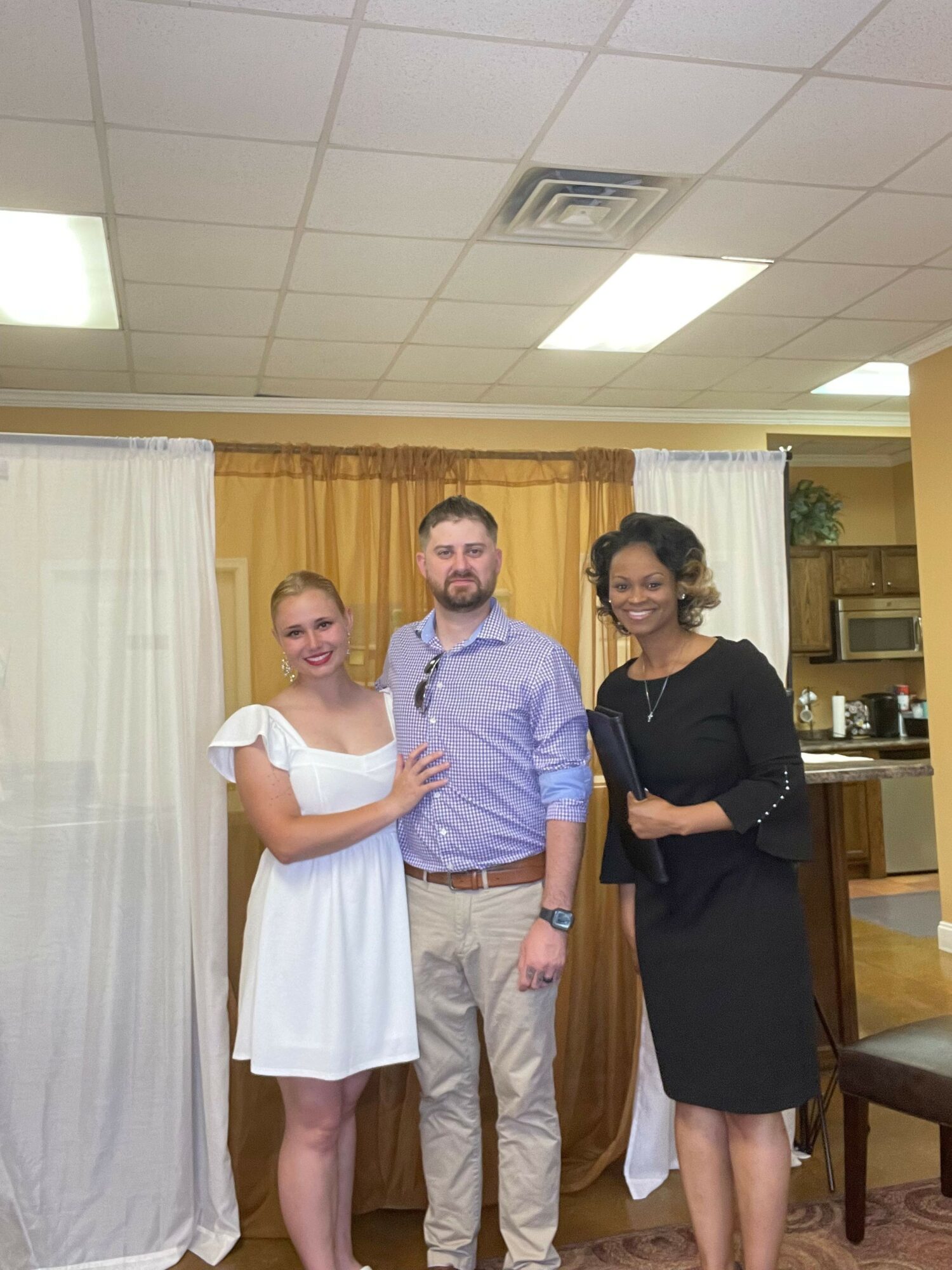 Three people standing indoors, two women and one man, smiling and posing for the photo.