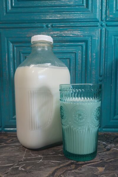 A large plastic bottle filled with milk and a glass with a light blue beverage on a dark marble surface, blue wooden background.