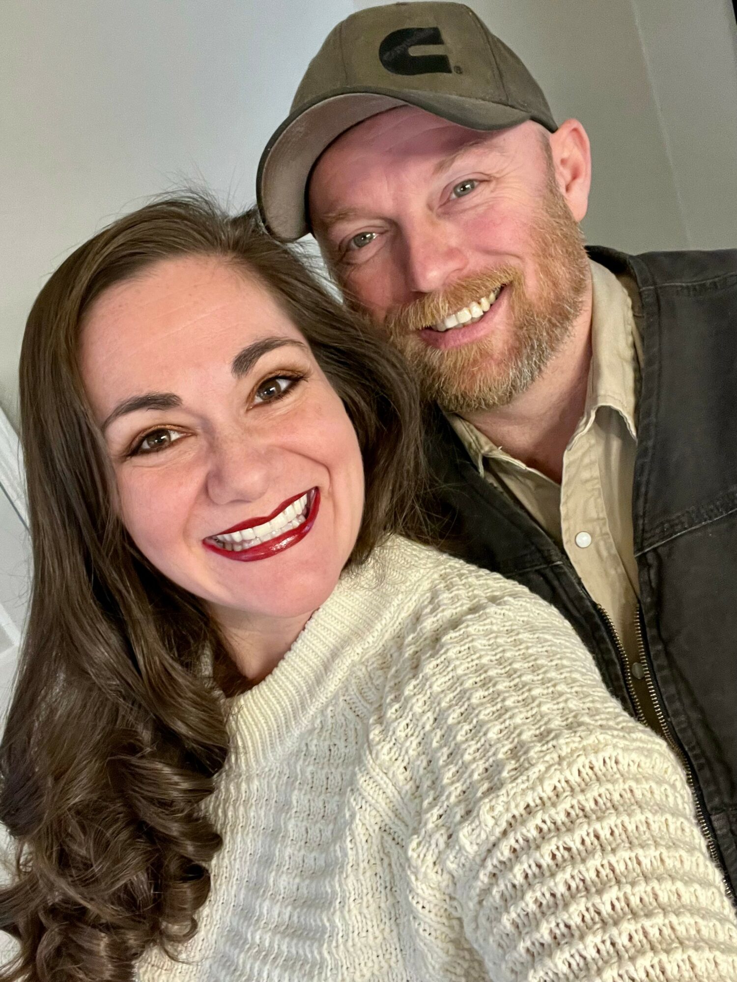 A smiling woman with long brown hair and a man with a beard and cap, both close together.