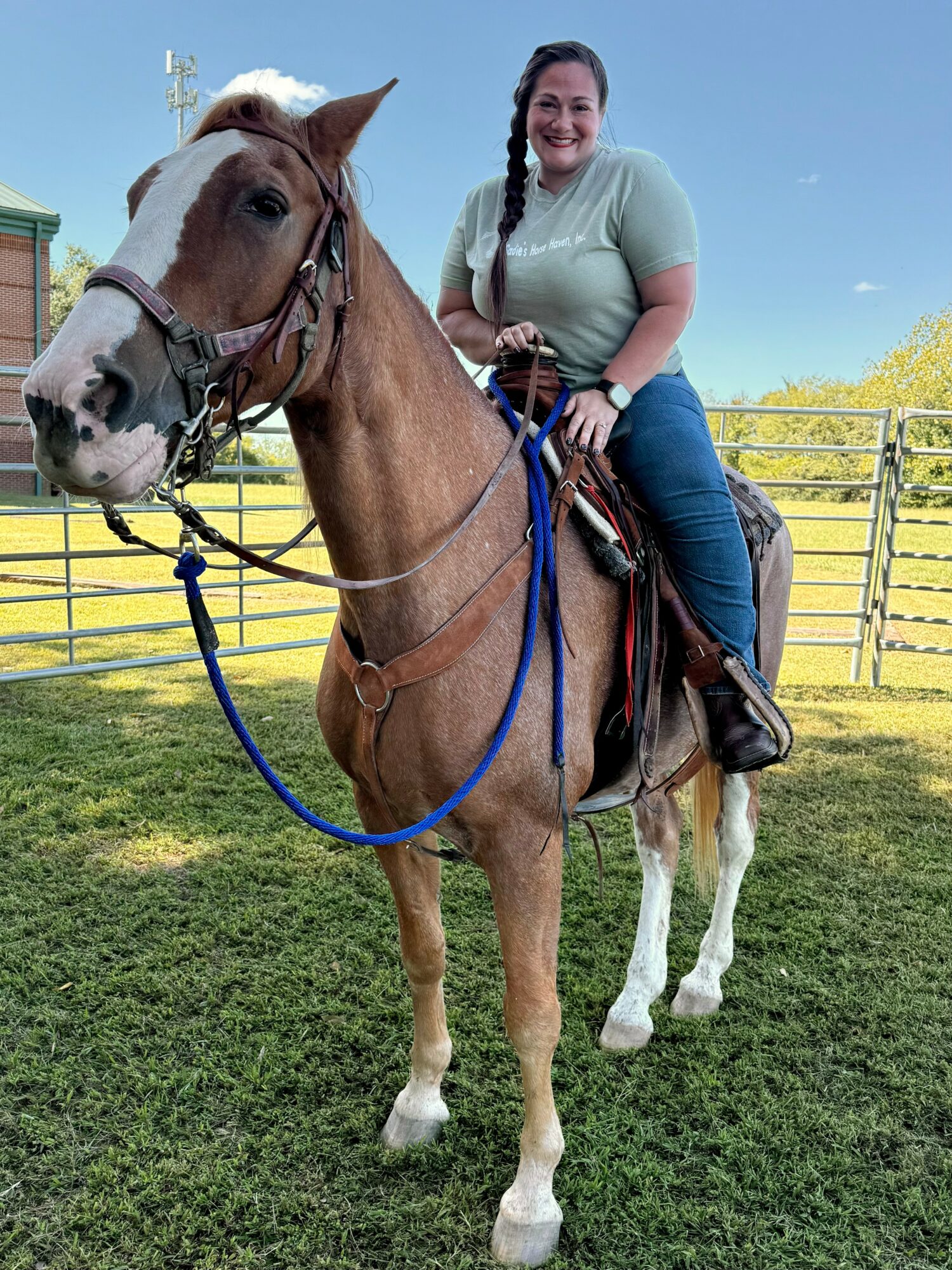 Woman riding a horse outdoors, smiling, with a fence and trees in the background.