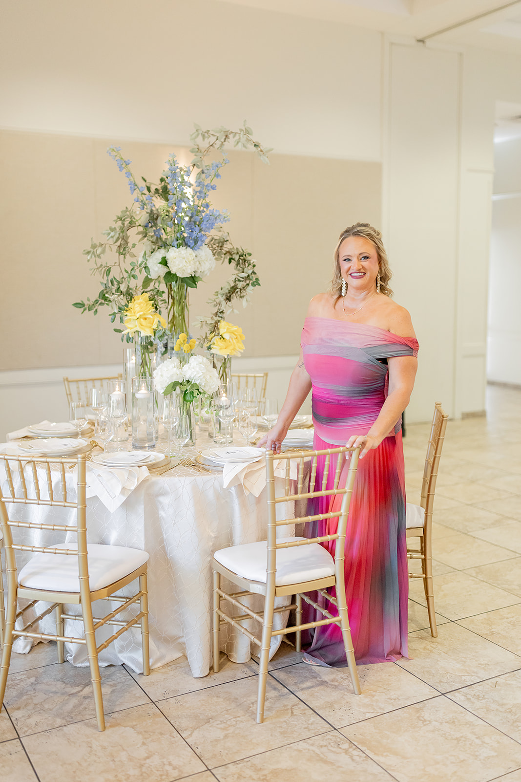 Woman in a colorful dress standing next to a decorated table with flowers in a bright room.