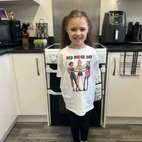 Young girl with long hair smiling in a kitchen, wearing a white T-shirt with a graphic and black pants.