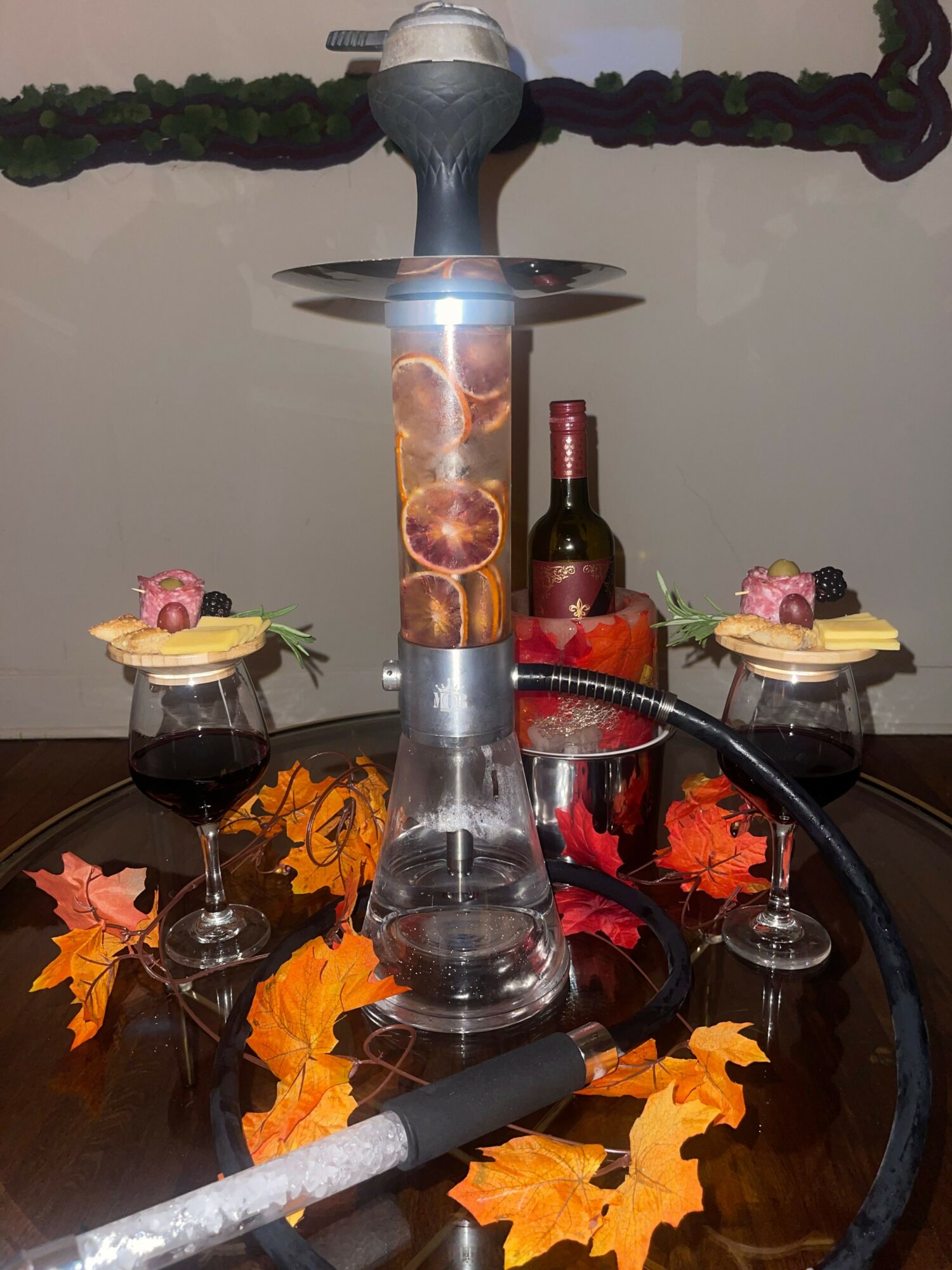 Decorative table with candles, wine bottle, glasses, and autumn leaves, viewed from the side.