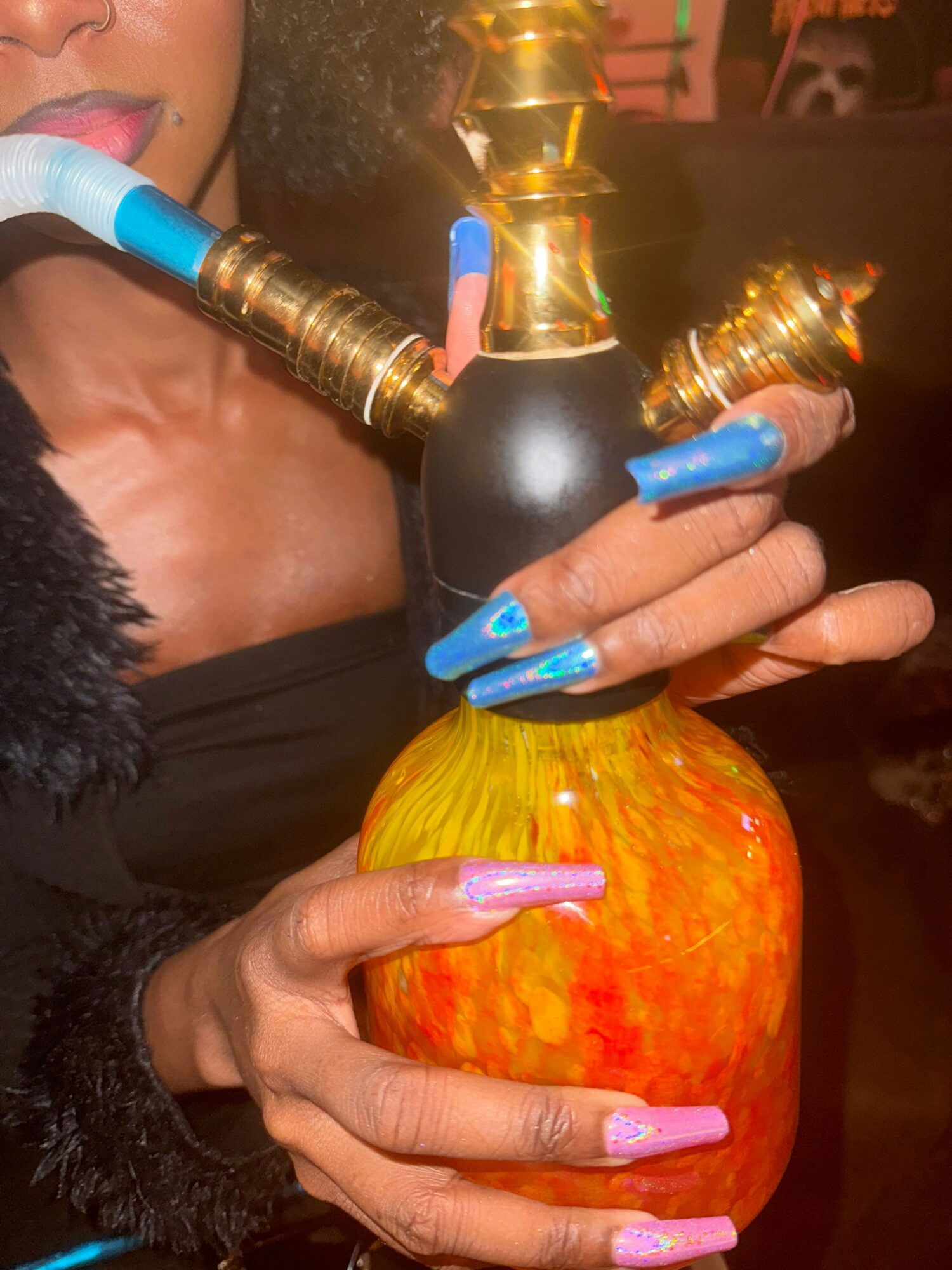 Person holding a colorful apple and a hookah pipe with long, painted nails.