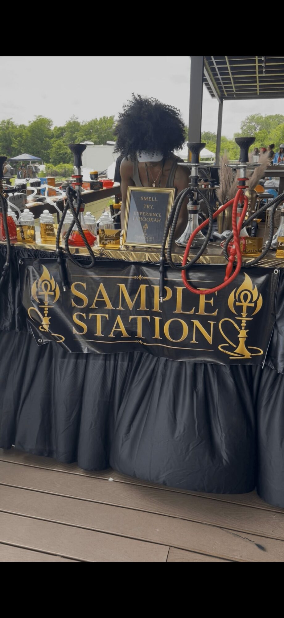 Sample station setup with a person behind a table, bicycles, and a black tablecloth, outdoors with trees in the background.