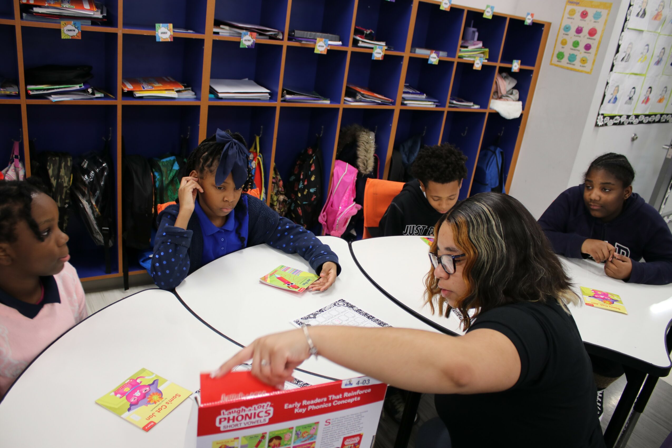 Teacher and students sitting at a table in a classroom, engaging with books and materials.