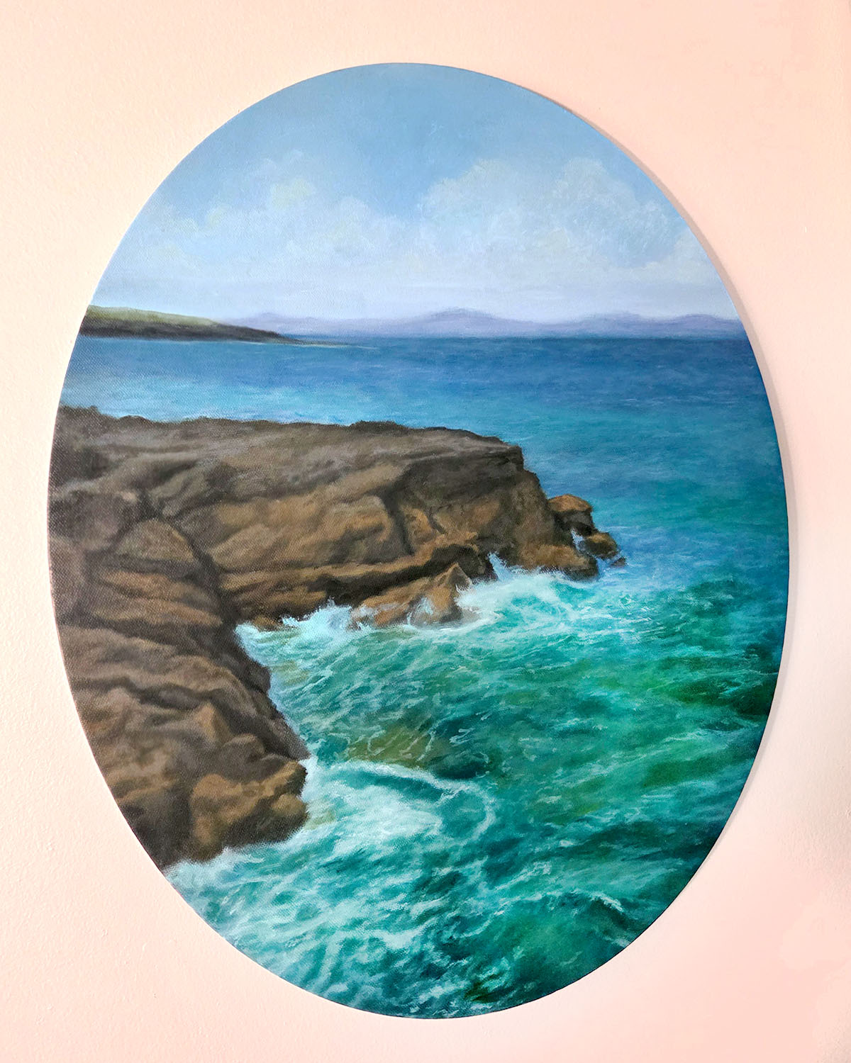 Painting of a rocky coastline with blue ocean waves and a distant horizon, framed in an oval shape.