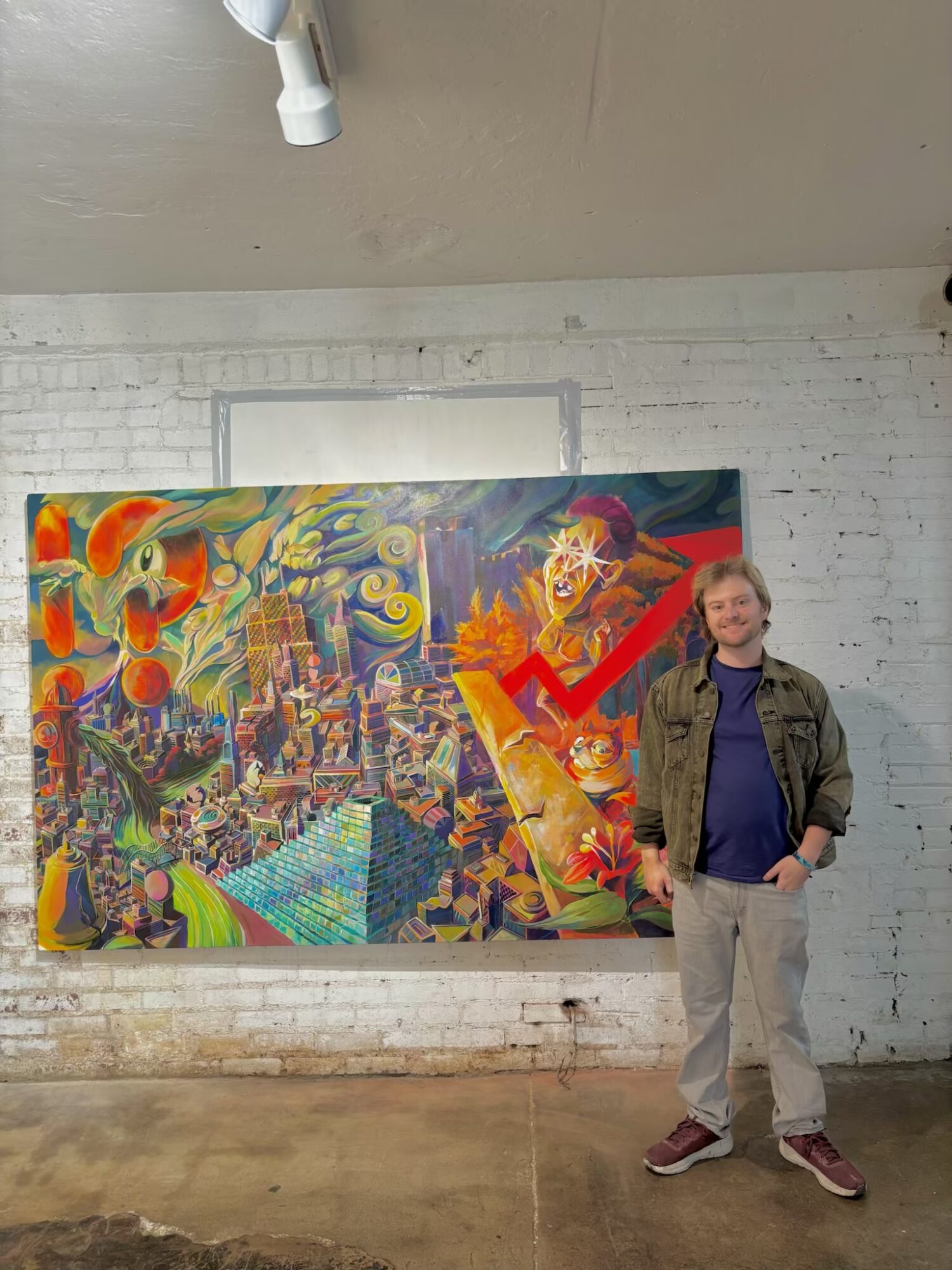 Person standing in front of colorful abstract painting on white brick wall, smiling, wearing a jacket and pants.