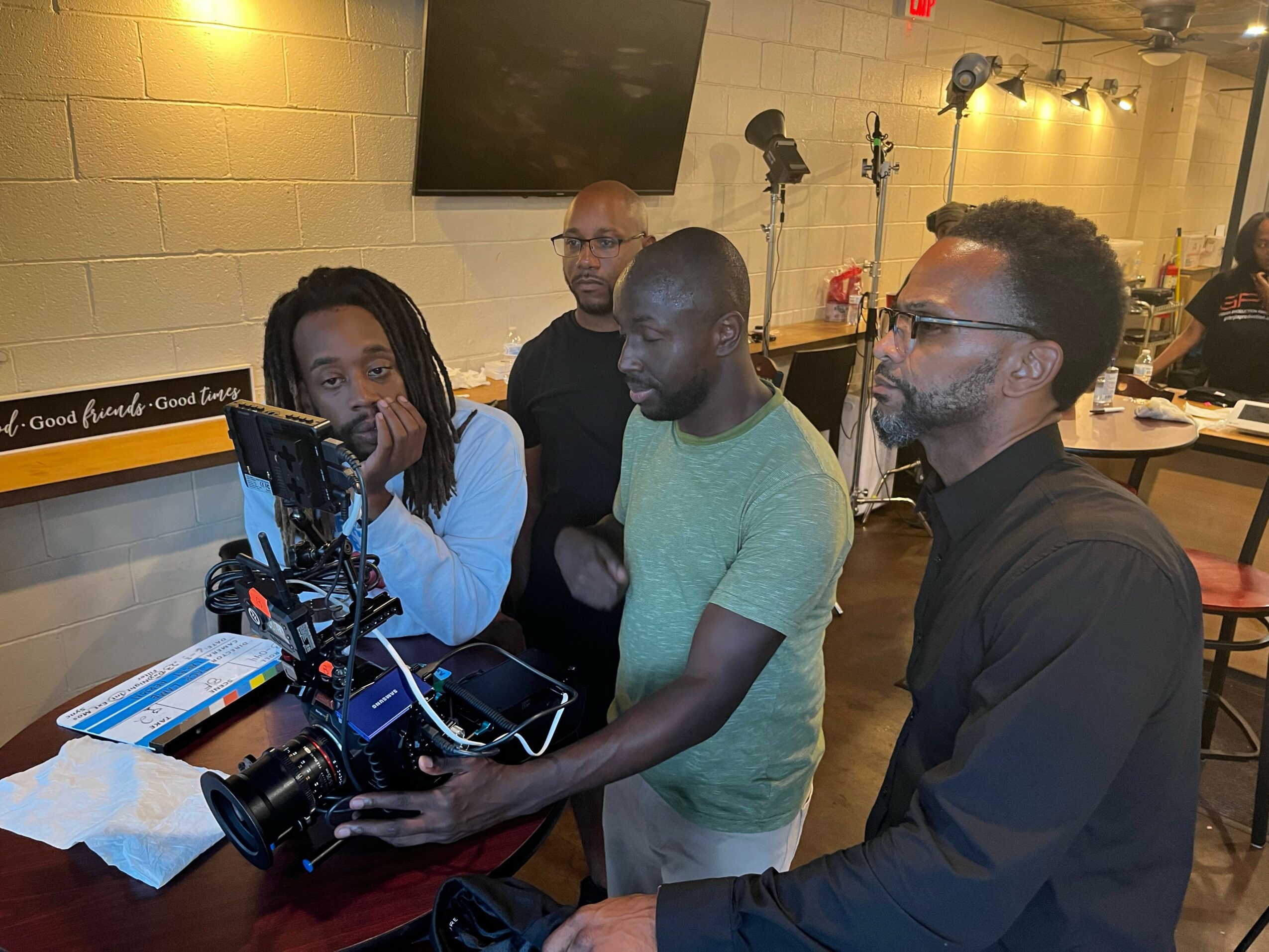 Group of people, including a person with a camera, gathered around a table in a room with warm lighting.
