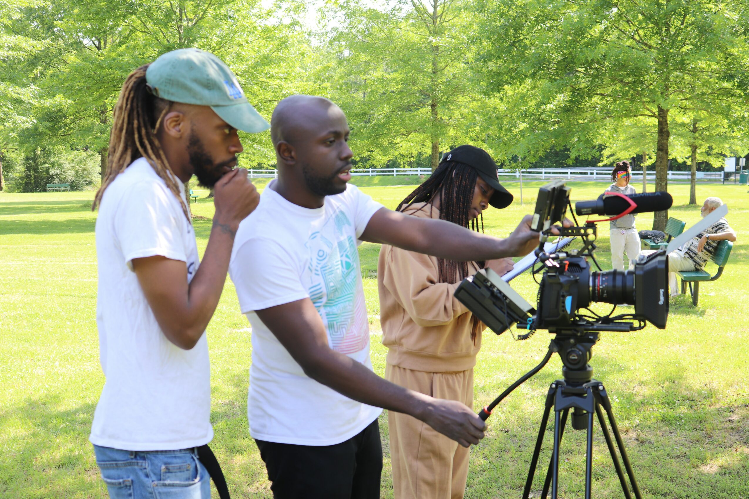Three people outdoors with a camera on a tripod, surrounded by green trees and grass.