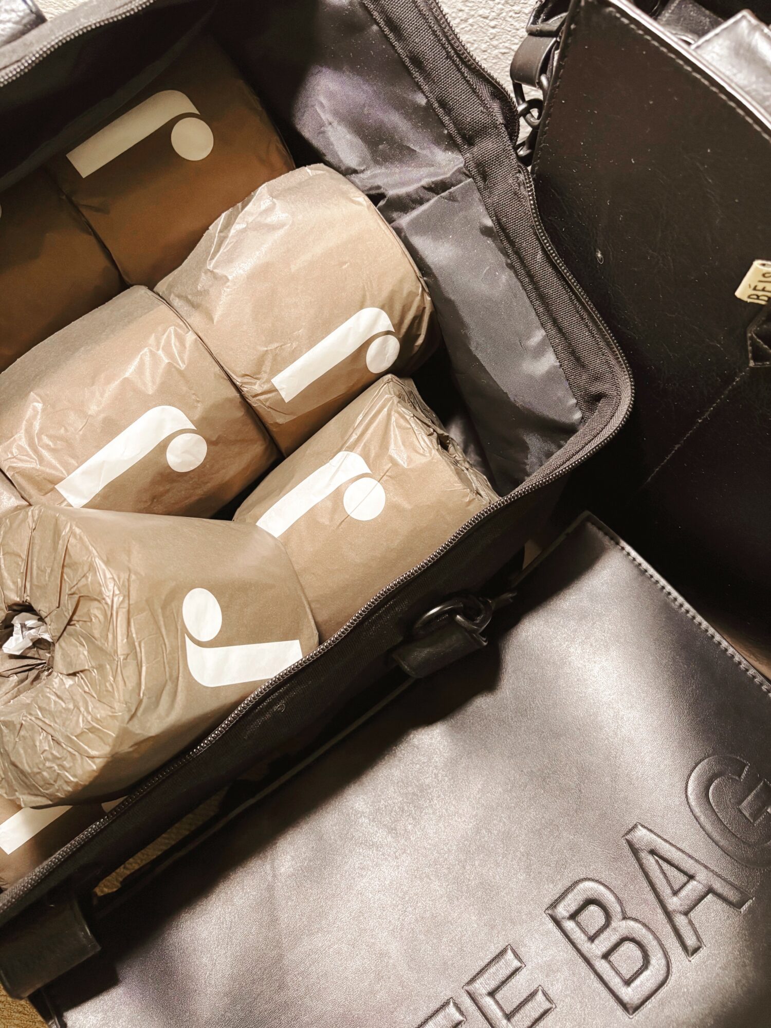 Open black suitcase with four wrapped packages inside, some with white tags, and a black bag nearby.