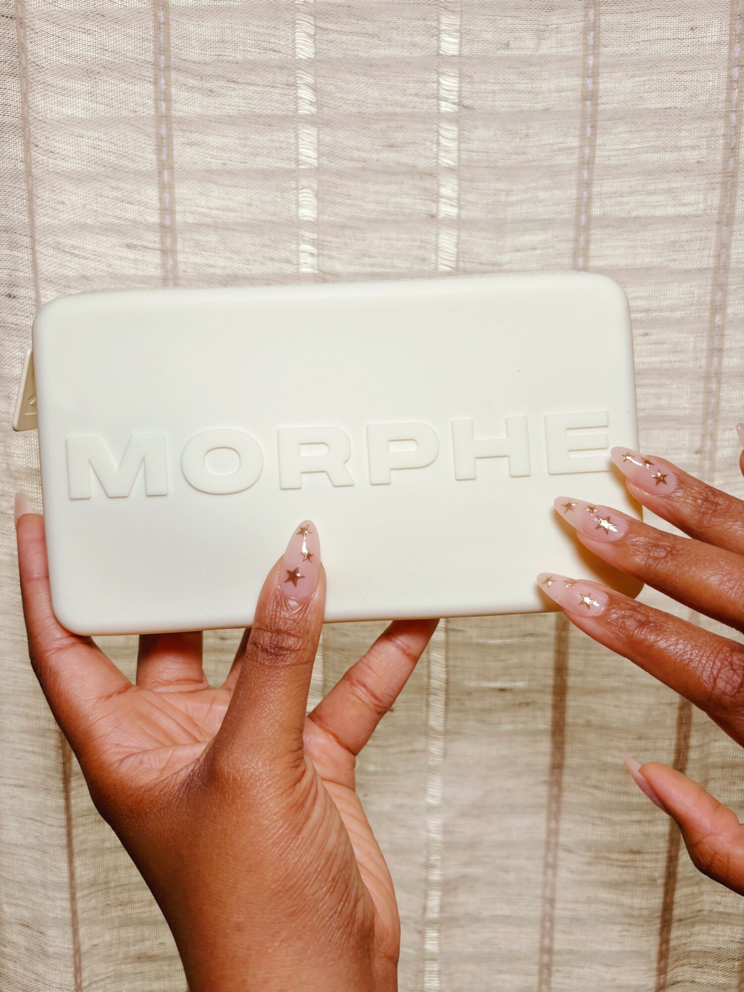 Two hands holding a white rectangular box with embossed text 'MORPHE' against a light-colored background.
