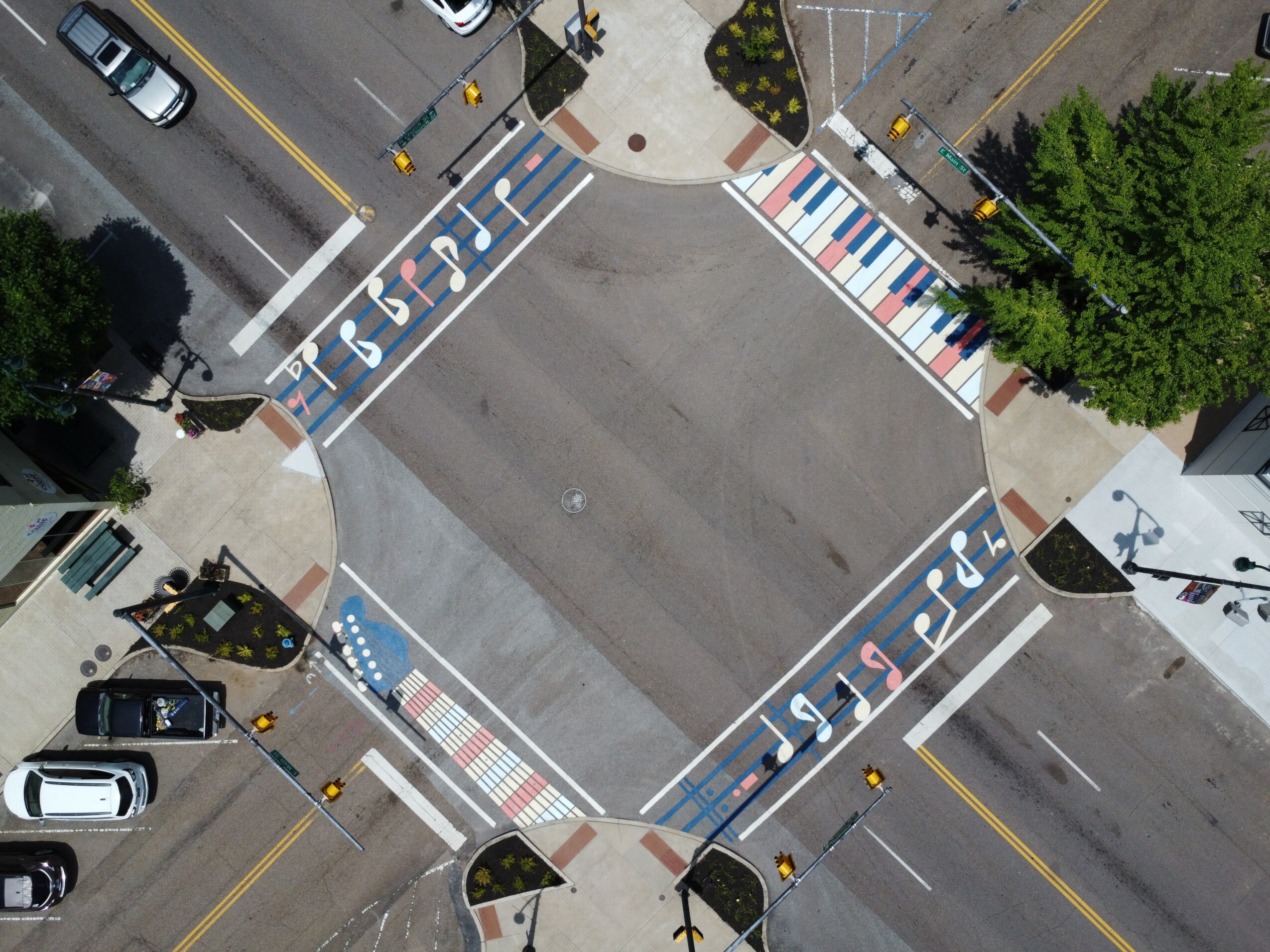Aerial view of a parking lot with designated handicapped spaces, crosswalks, and surrounding streets with cars and trees.