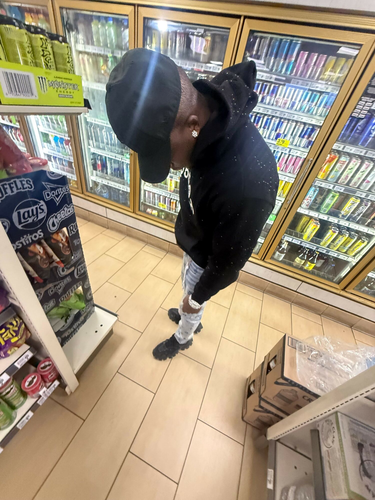 Person shopping in a convenience store, looking at refrigerated items, with shelves and a floor visible.