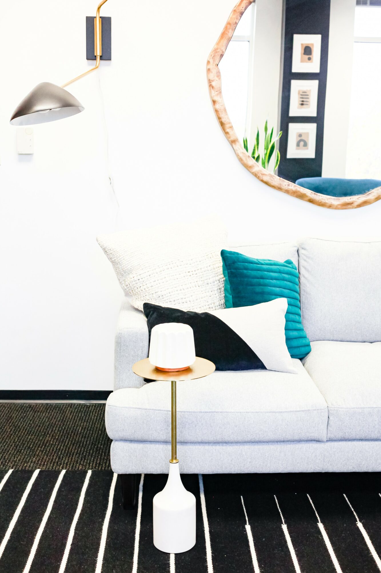 Living room with white sofa, blue pillows, round mirror, and wall art, with a side table and black and white striped rug.