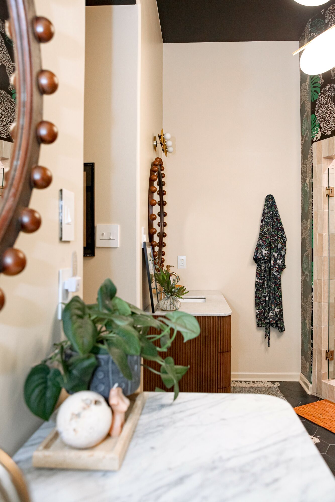 View of a hallway with a coat hanging on the wall, a small cabinet, and a plant on a marble surface.