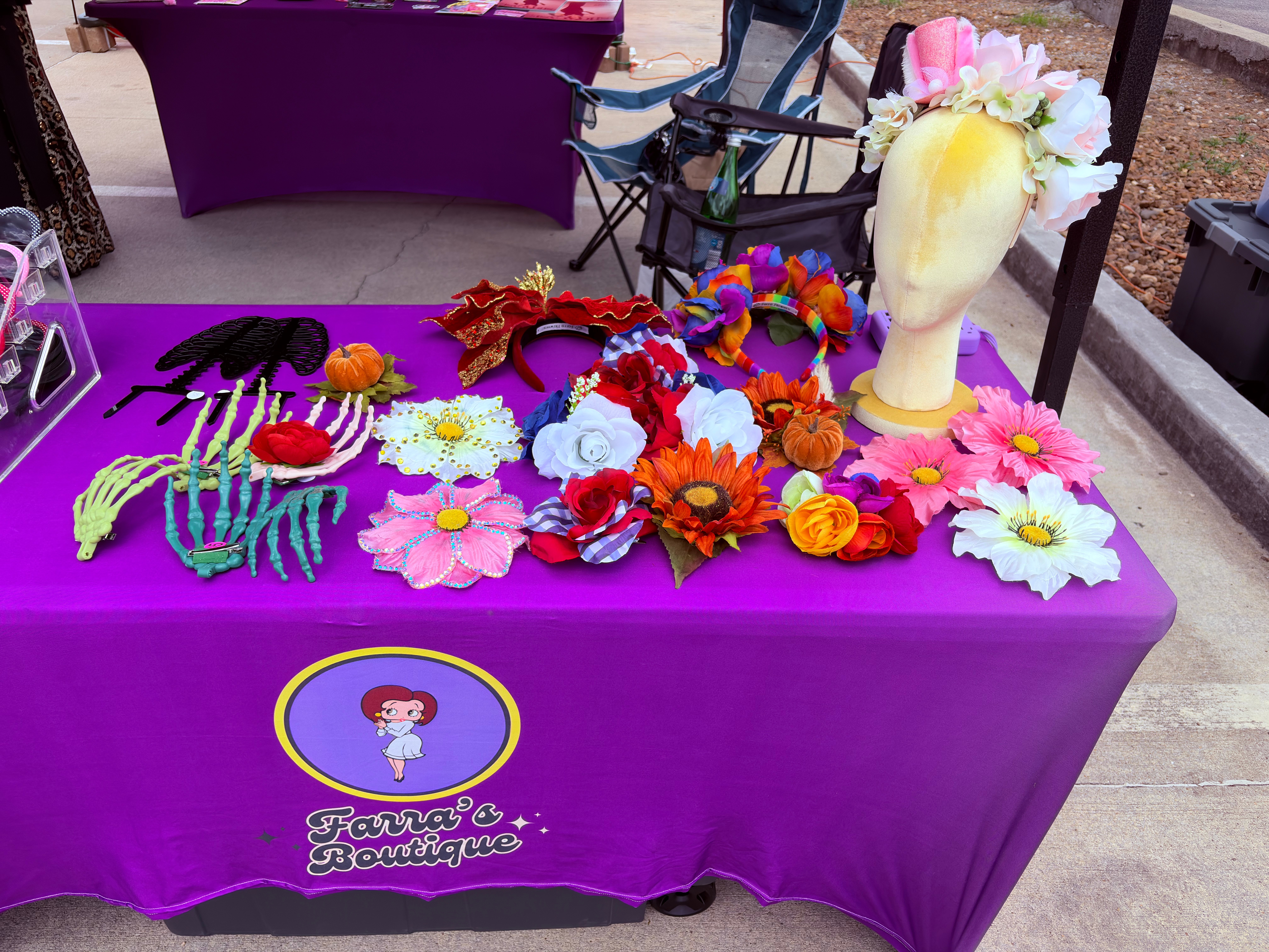 Purple tablecloth with colorful flower accessories and a white vase with flowers, outdoor setting, cartoon character logo, 20 words.