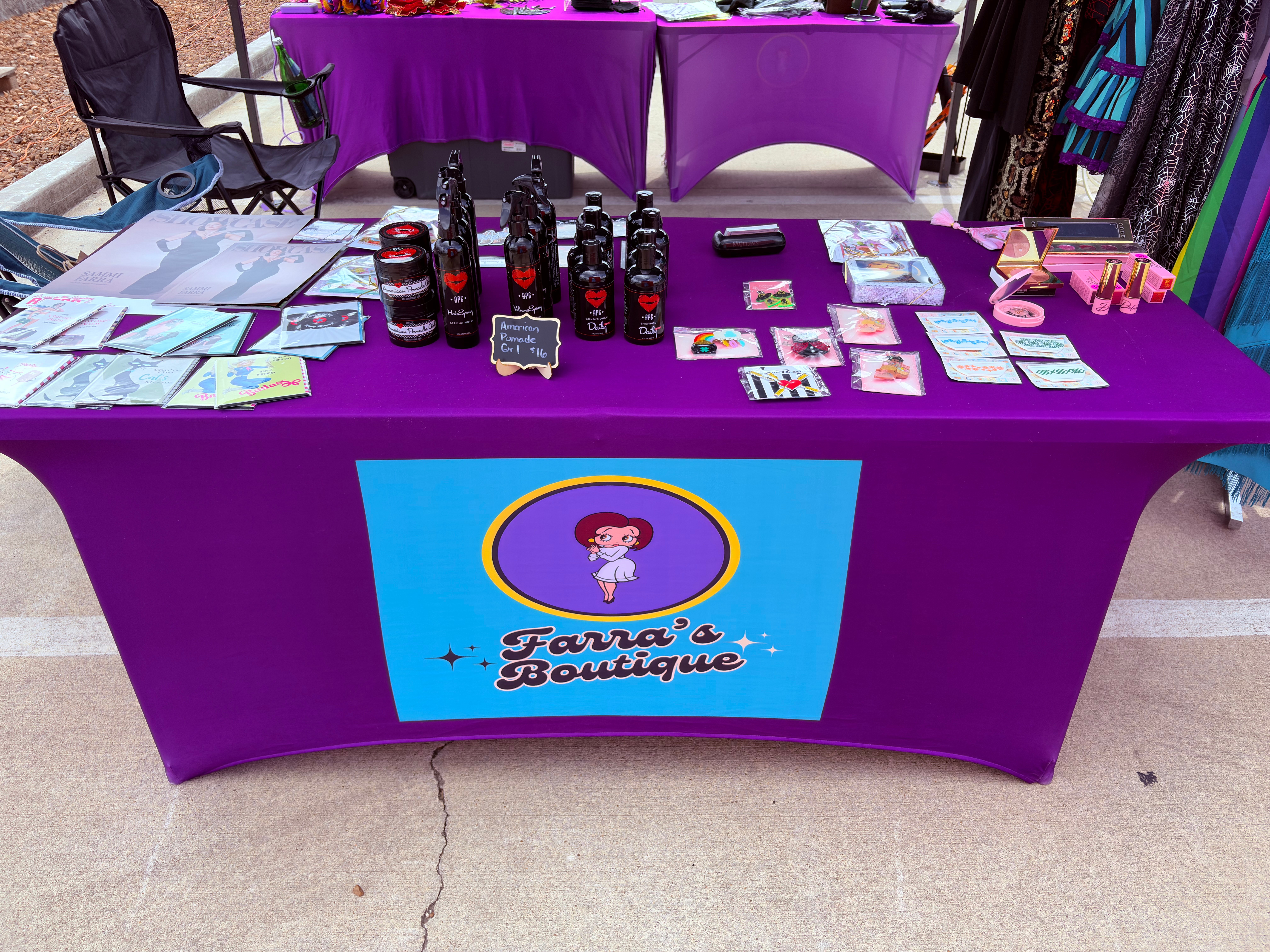 Table with products and promotional materials, purple tablecloth, and a sign reading 'Faru's Boutique' with a cartoon girl, at an outdoor event.
