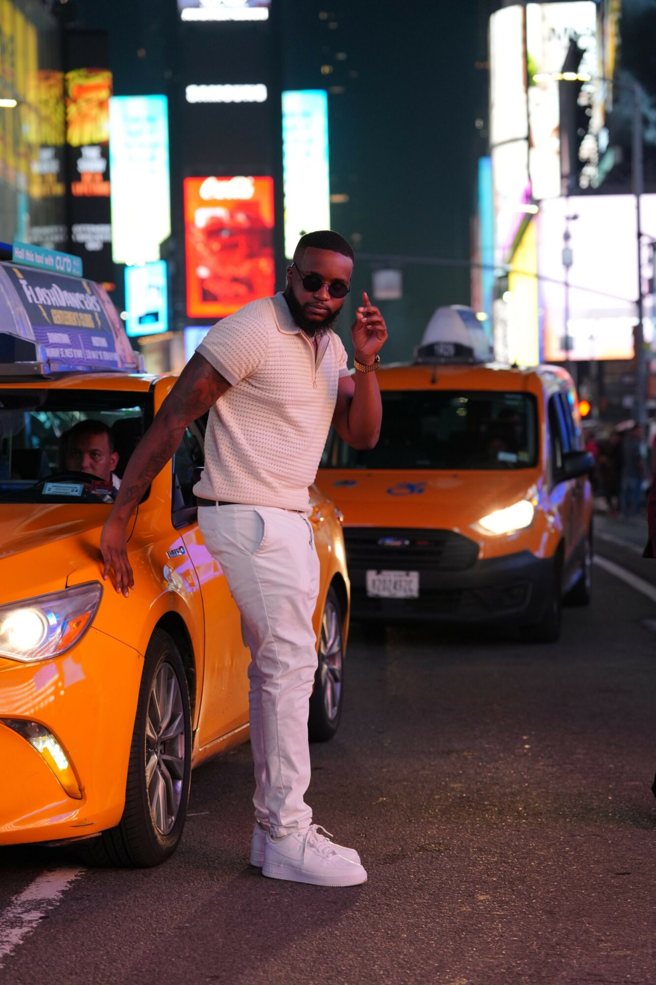 Person standing next to a yellow sports car in a city at night, with bright lights and digital billboards in the background.