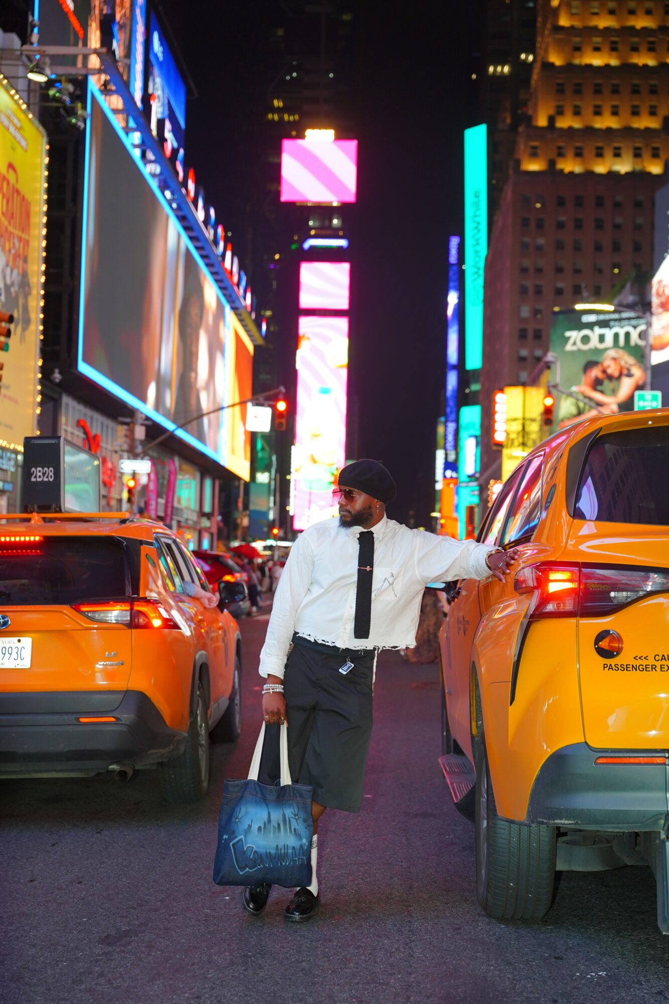 Man in white shirt and black tie walking in Times Square at night, surrounded by bright neon lights and taxis.