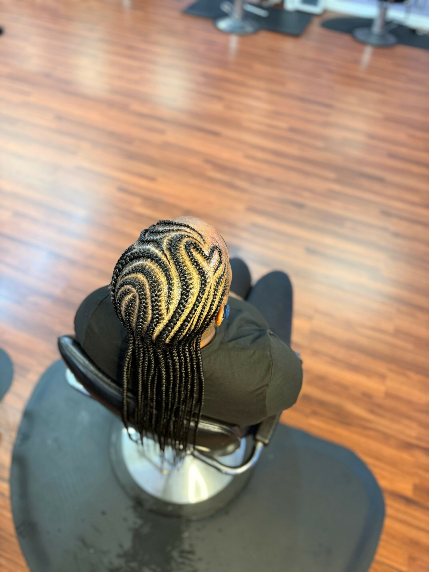Top-down view of a person with braided hair sitting in a salon chair on a wooden floor.