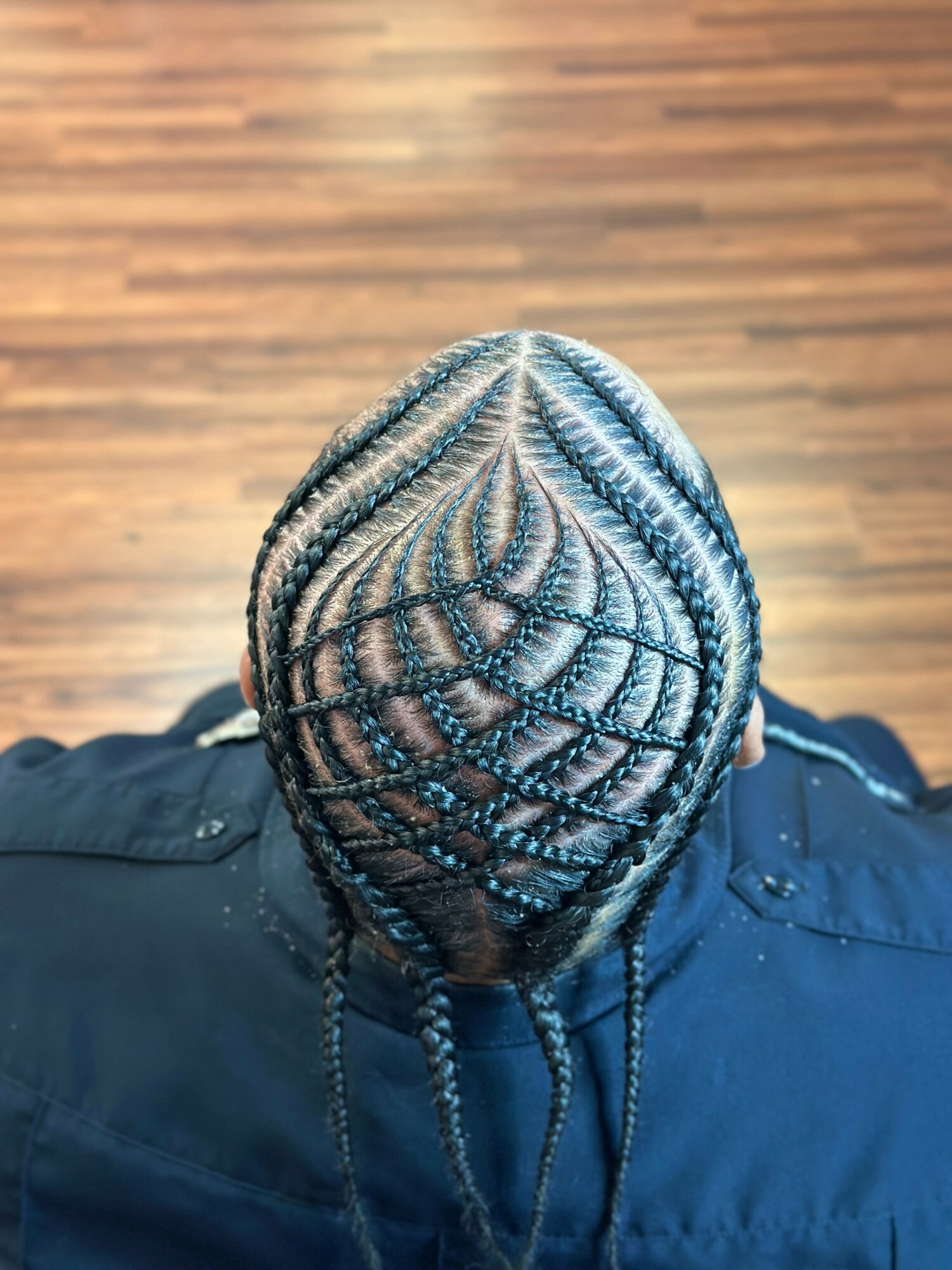 Top view of a person's head with intricate braided hairstyle, seen from above, with a wooden floor background.