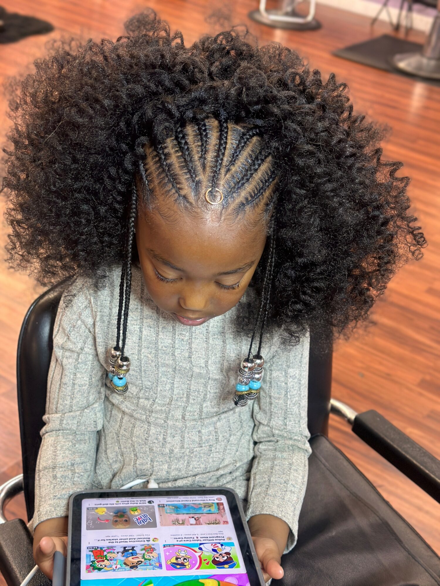 Young girl with braided hair and curly hair, looking at a tablet, sitting in a chair indoors.