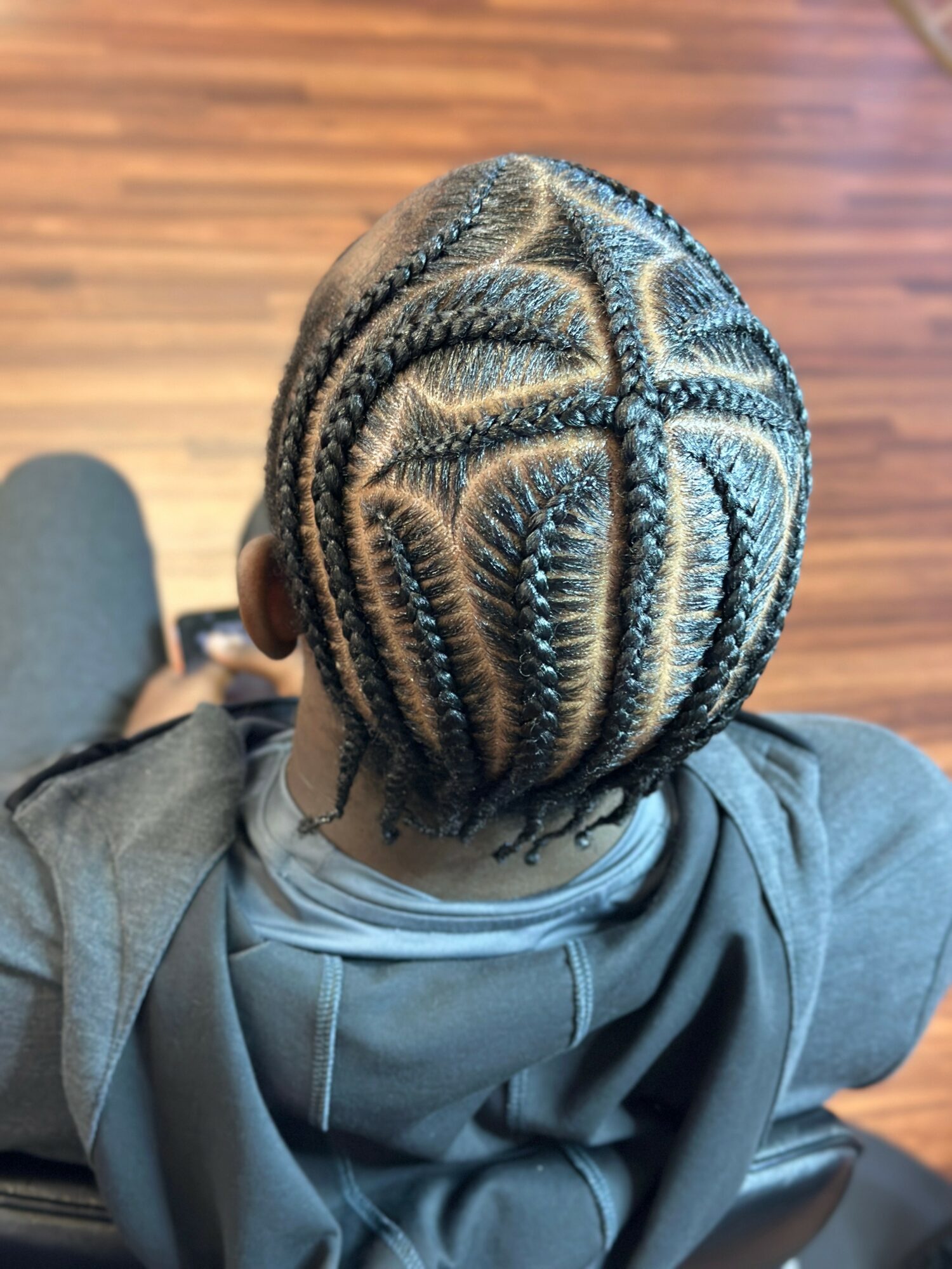 Top view of a person with intricate braided hairstyle on a wooden floor, wearing a gray hoodie.