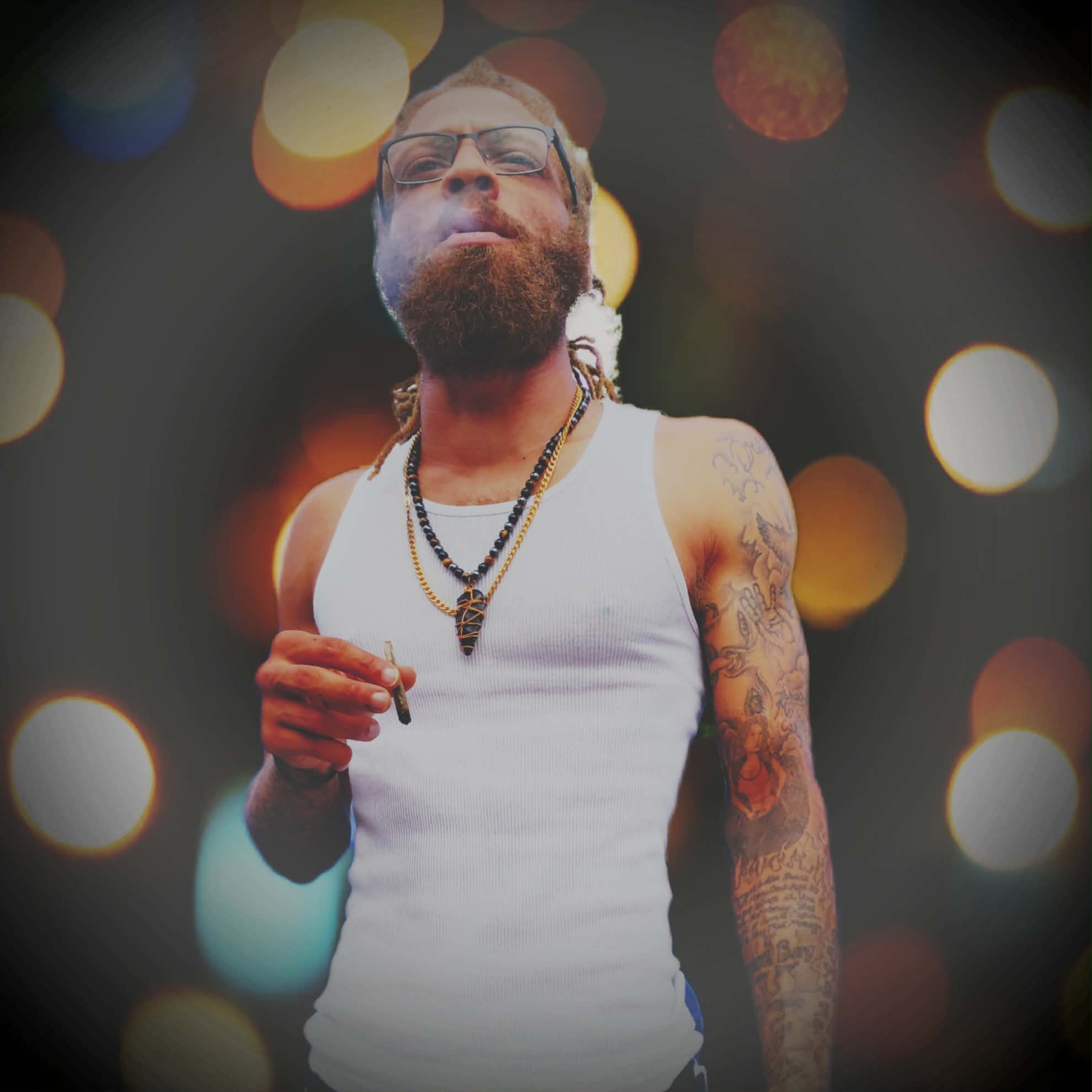 Man with glasses, beard, tattoos, wearing a white tank top, holding a cigarette, with blurred colorful lights background.