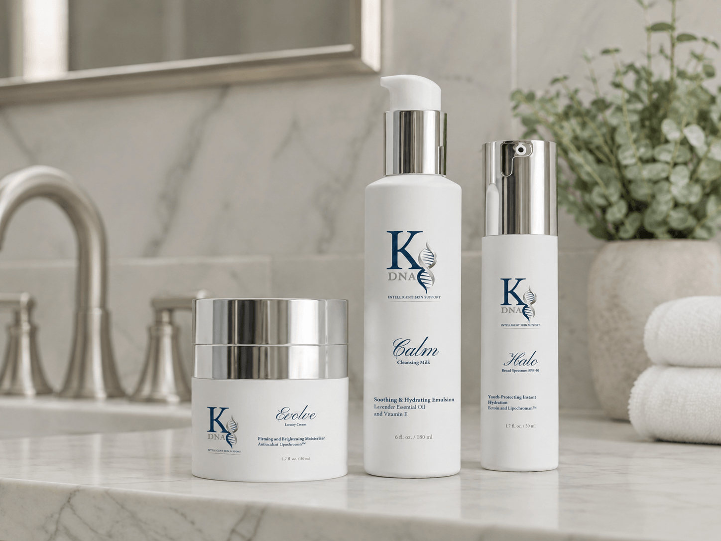 Three skincare products with white and silver packaging on a marble bathroom counter, with a plant and towels in the background.