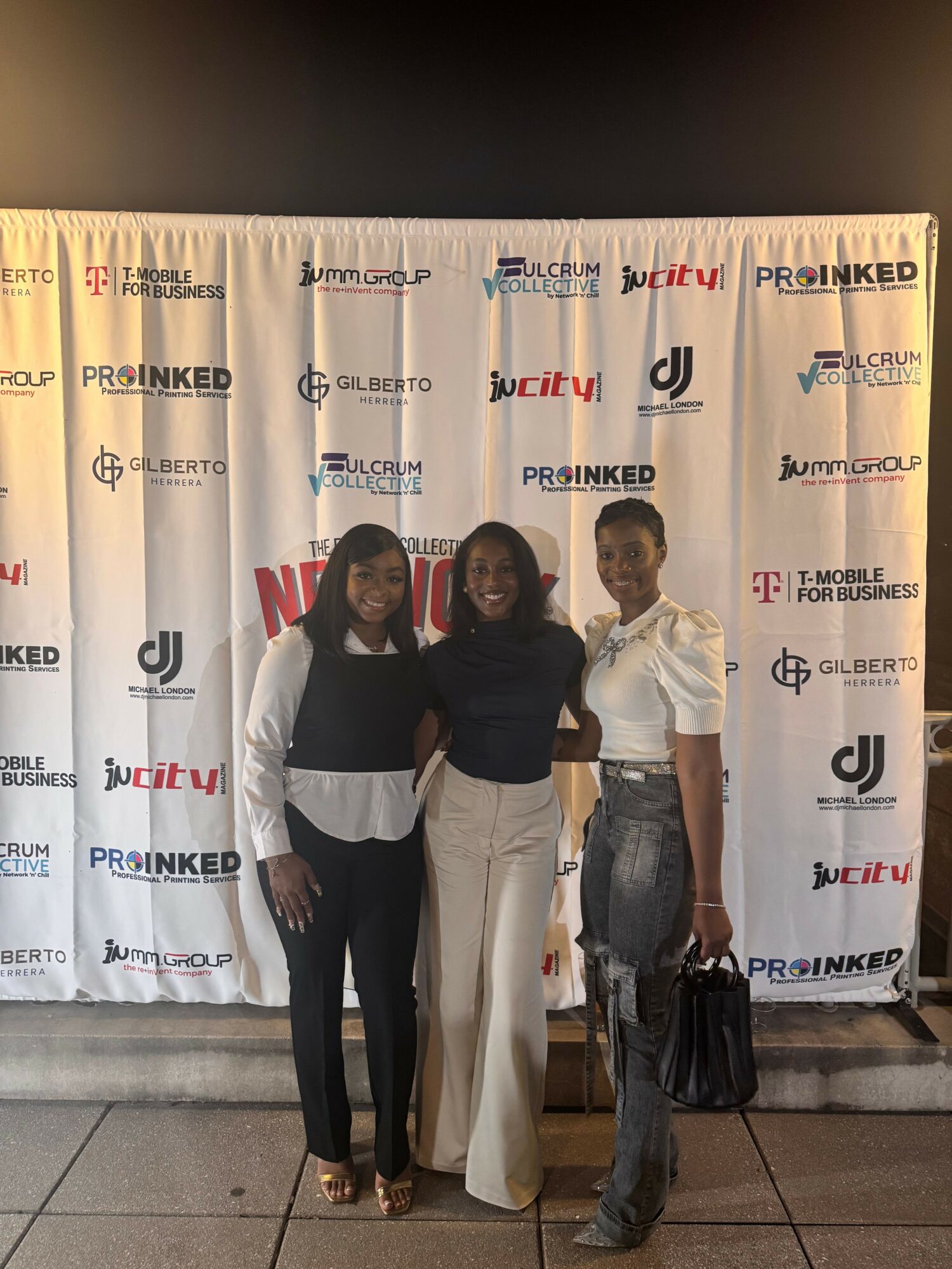 Three women standing in front of a backdrop with logos, posing for a photo indoors.