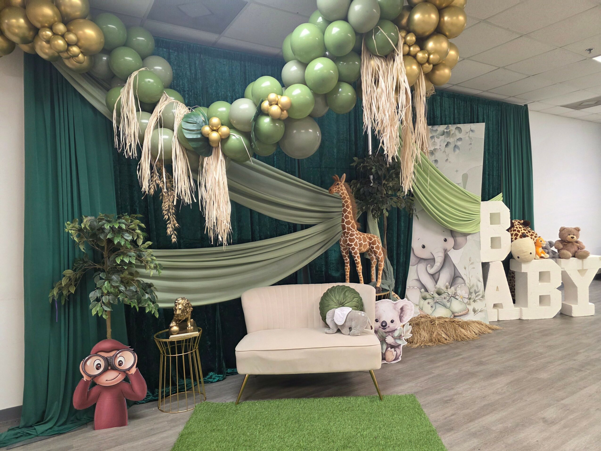 Decorative setup with balloons, plants, and plush toys against a dark curtain backdrop.
