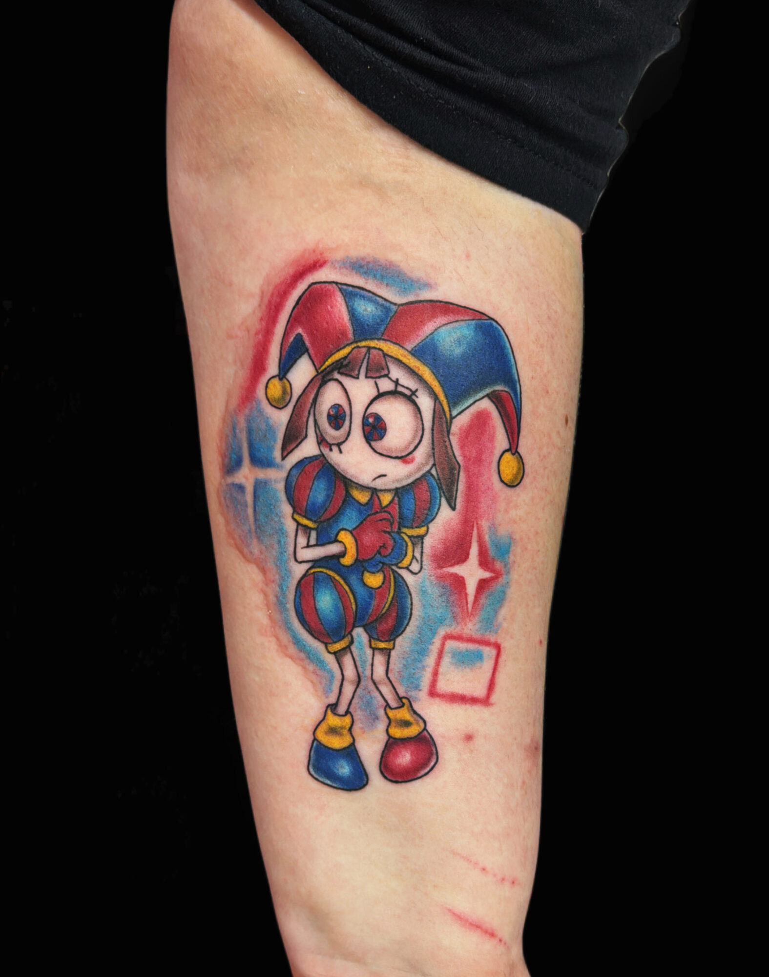 Tattoo of a cartoon character in a jester costume with a hat, large eyes, and colorful clothing on a person's thigh.