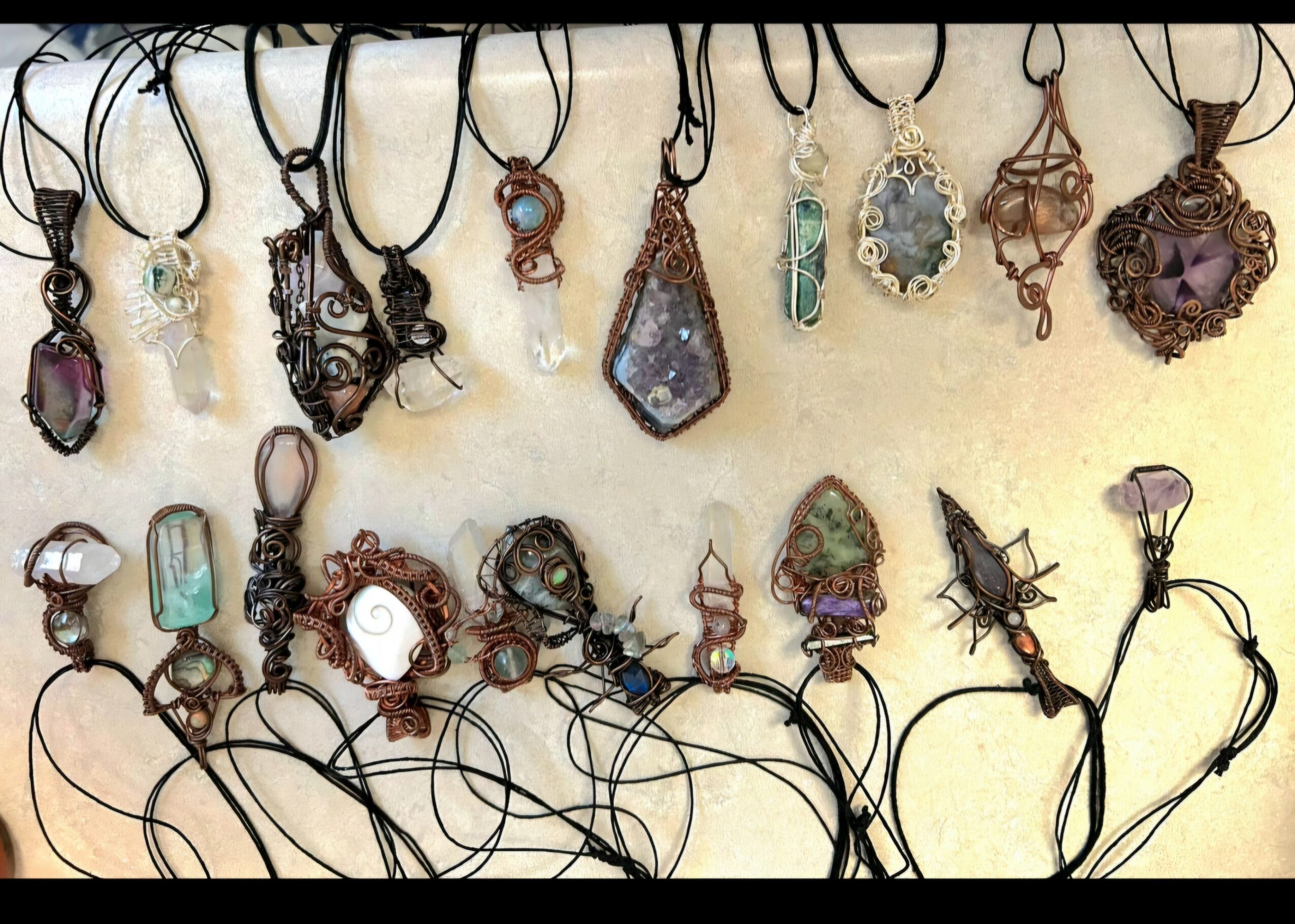 Collection of necklaces with various pendants hanging on a display, some with stones and intricate designs.