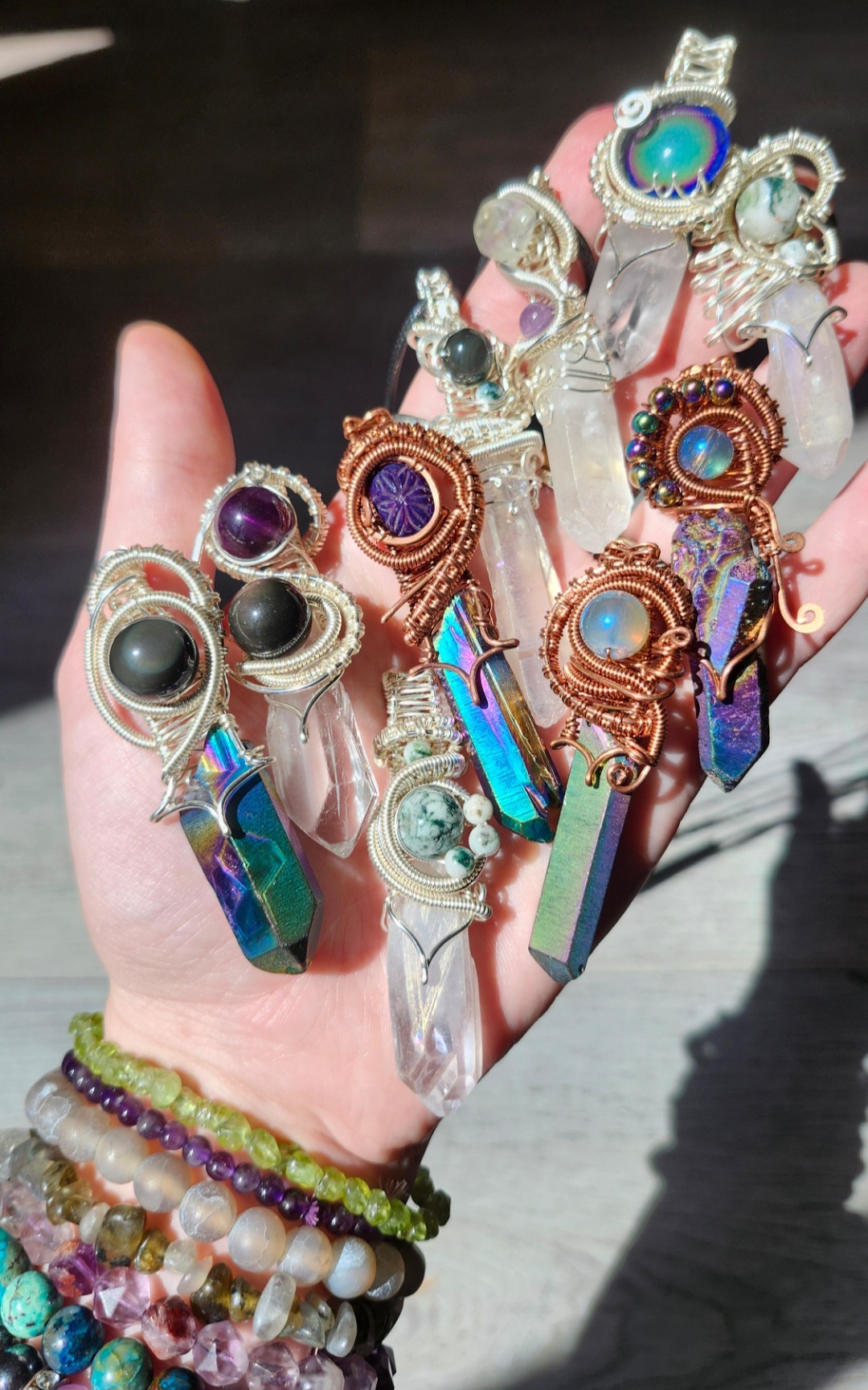 Hand with multiple colorful rings and bracelets, some with large stones and iridescent elements, against a dark background.