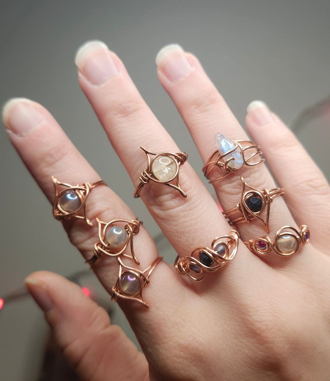 Hand with multiple rings featuring various gemstones and designs, against a neutral background.