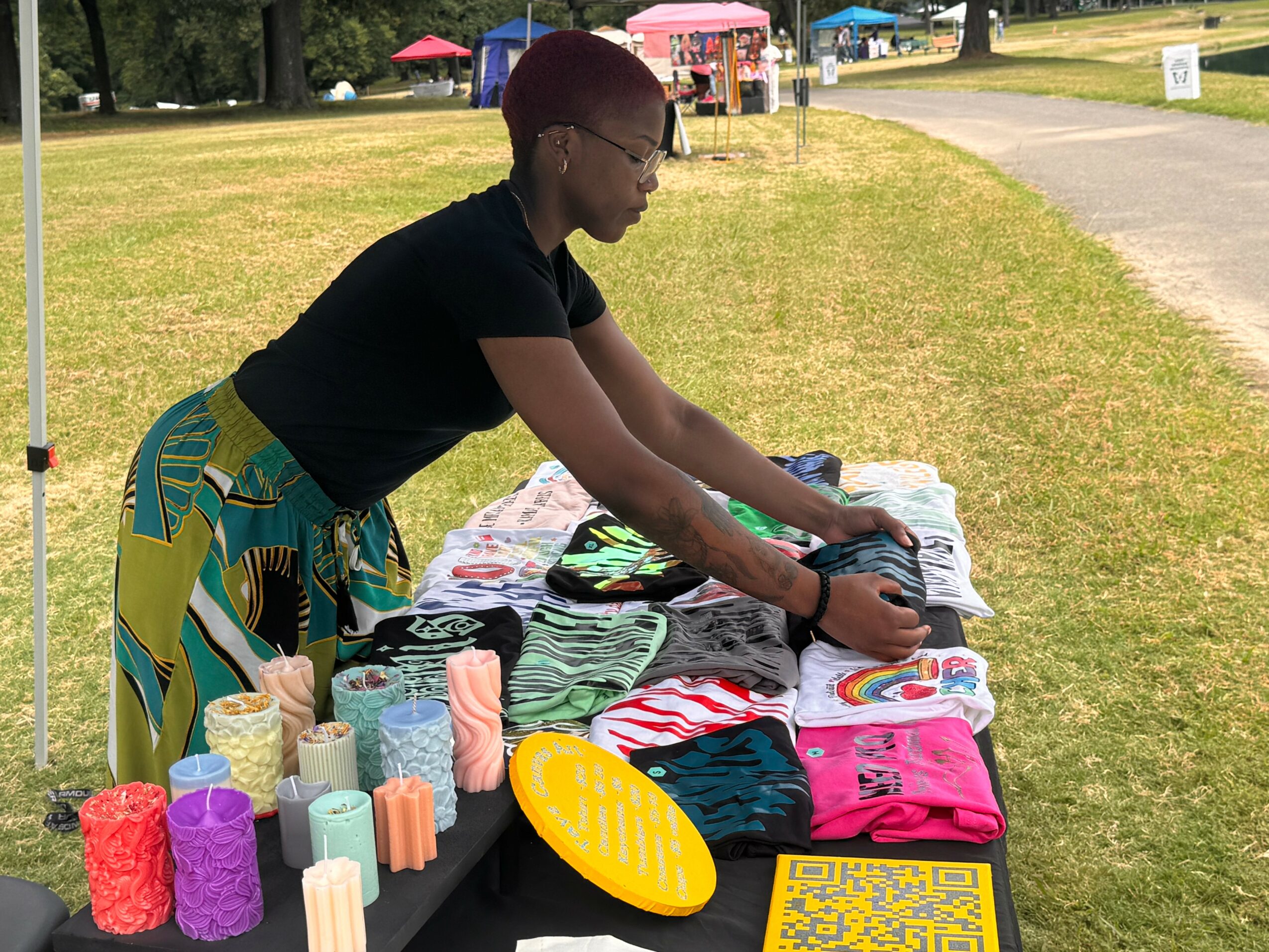 Person with short hair and glasses arranging clothes on a table outdoors, with colorful items and a yellow plate nearby.