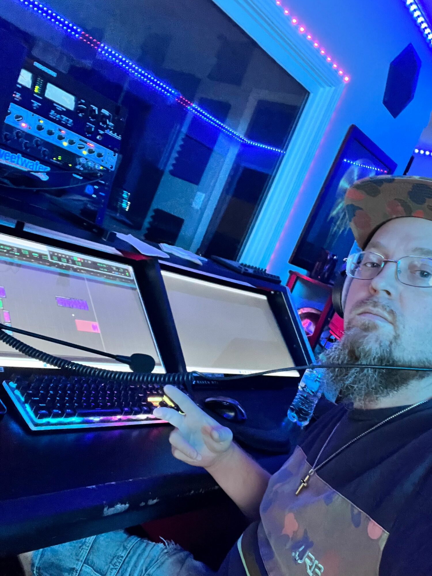 Person with glasses and beard working at a computer in a room with blue LED lights, wearing gloves.