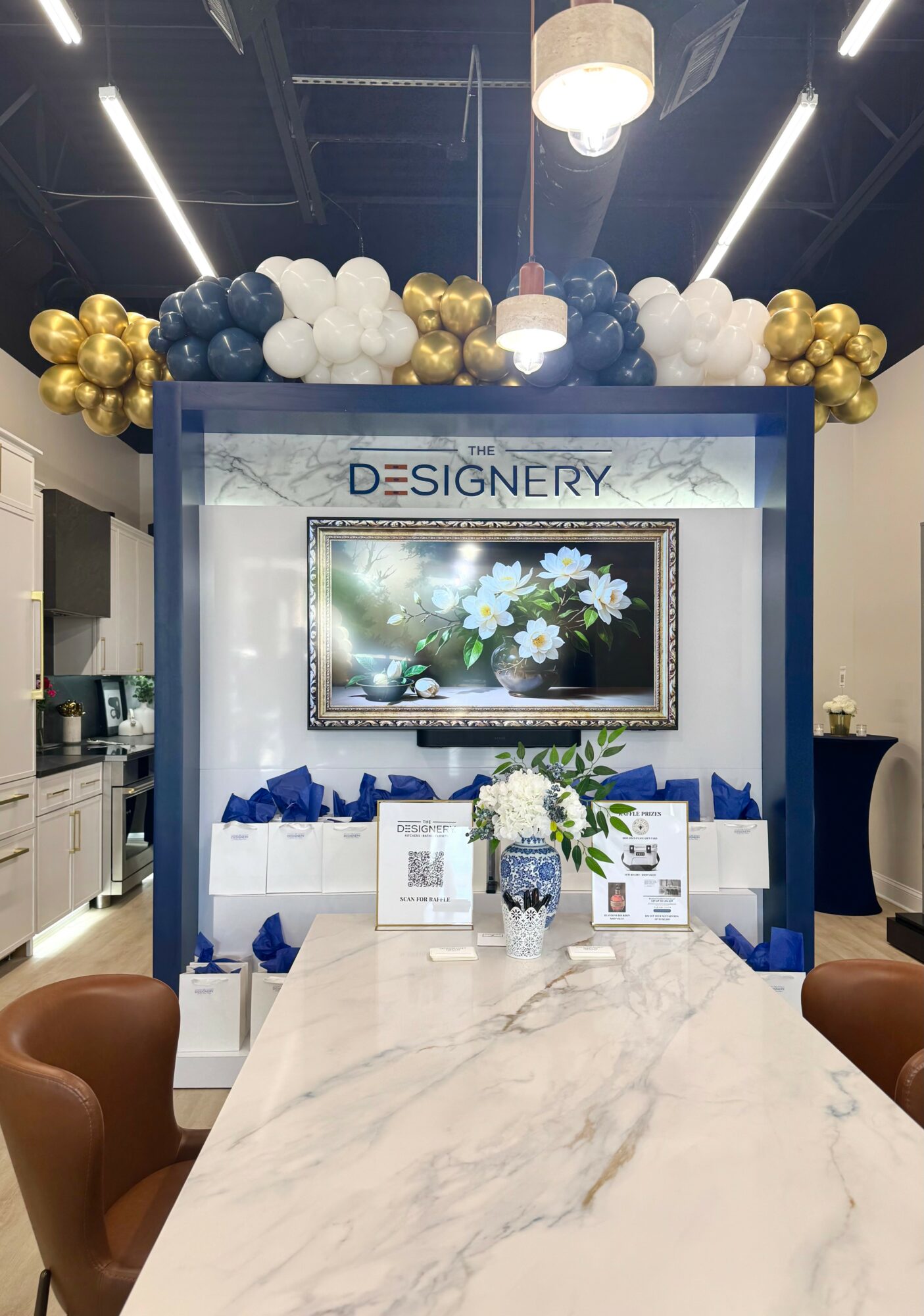 Decorative display with balloons, a framed digital screen, and a table with flowers and informational materials.